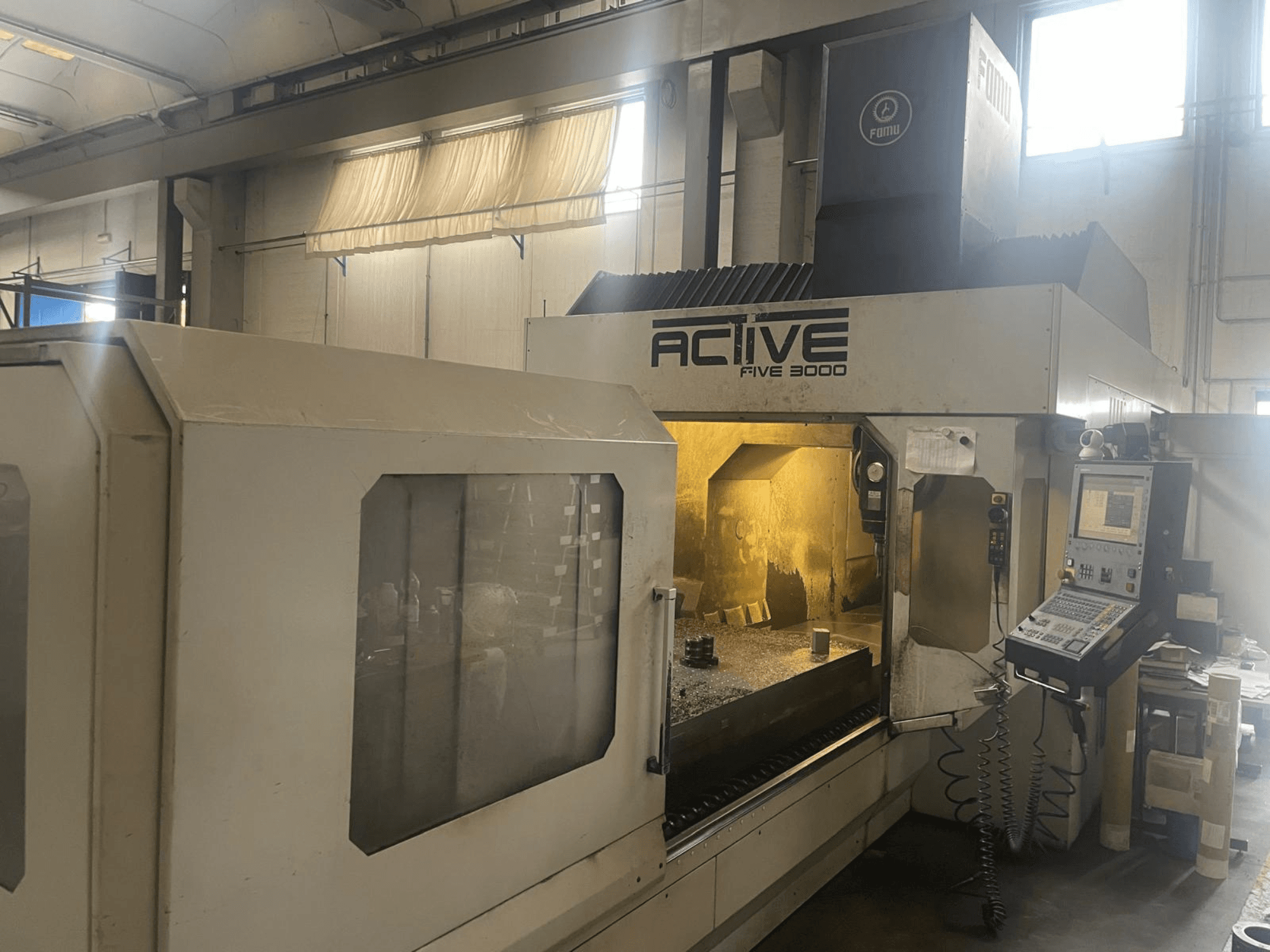 CNC staklių "ACTIVE Five 3000" priekinis vaizdas, rodantis valdymo skydelį ir darbo zoną su viduje esančia iš dalies apdirbta detale.