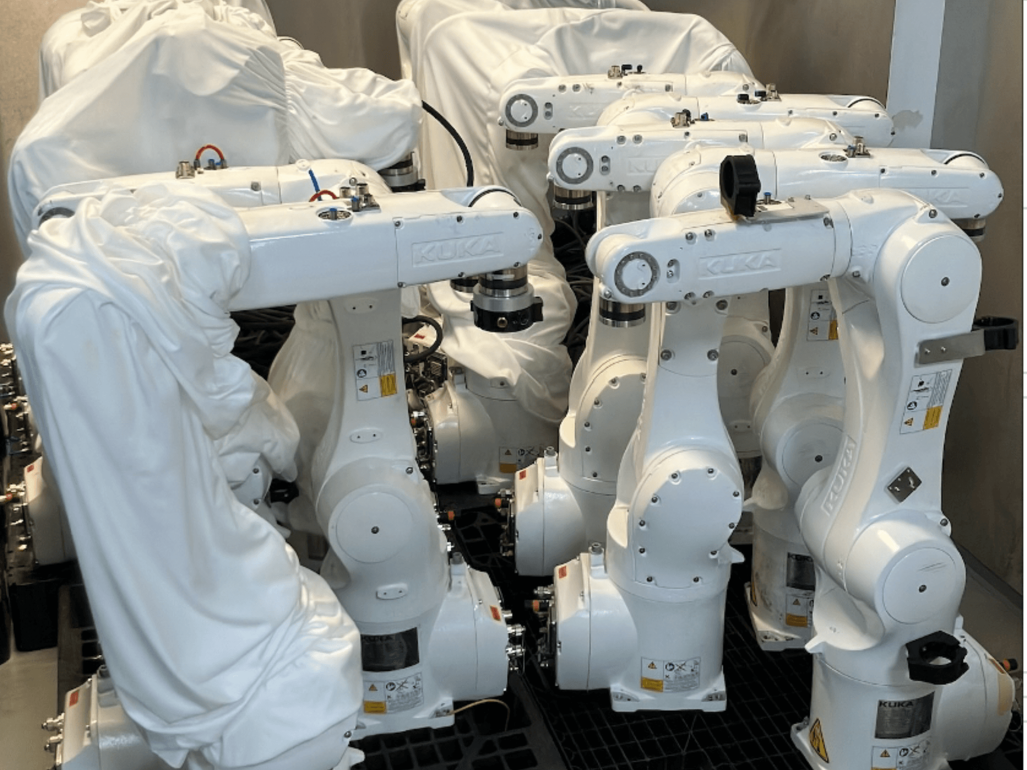 Iš priekio žiūrint į iš dalies audiniu aptrauktas roboto KUKA KR 10 R900-2 rankas, išryškėja jų elegantiškas baltas dizainas ir techninės detalės.