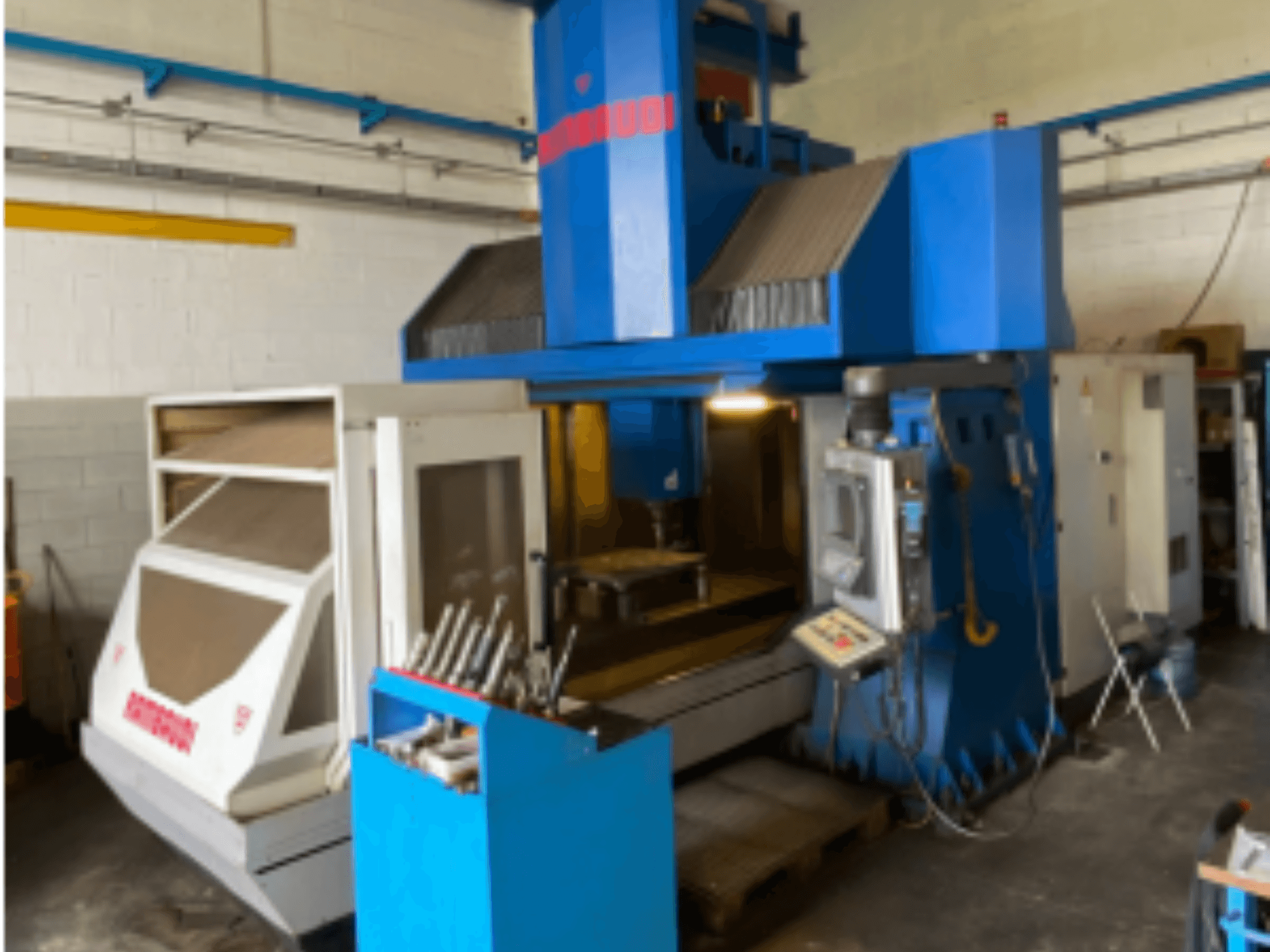 Vertikalusis apdirbimo centras Rambaudi RF103, priekinis vaizdas, kuriame matyti valdymo įtaisai, įrankių laikymo vieta ir apdirbimo zona. Mėlynos ir baltos spalvos išorė.