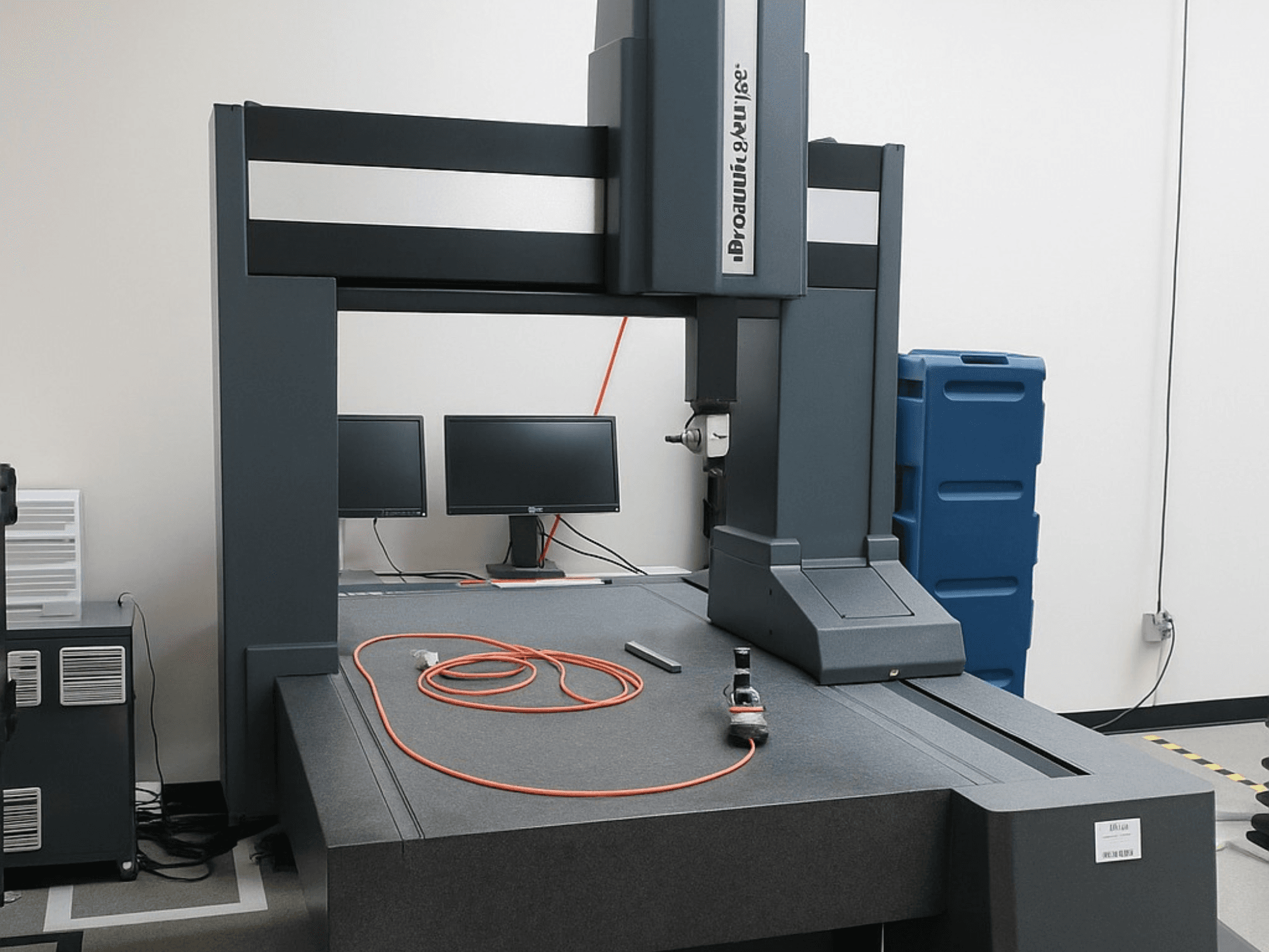 "Brooks Automation" koordinačių matavimo mašina su dviem monitoriais, vaizdas iš priekio, pilkas stalviršis ir matavimo įrankiai.