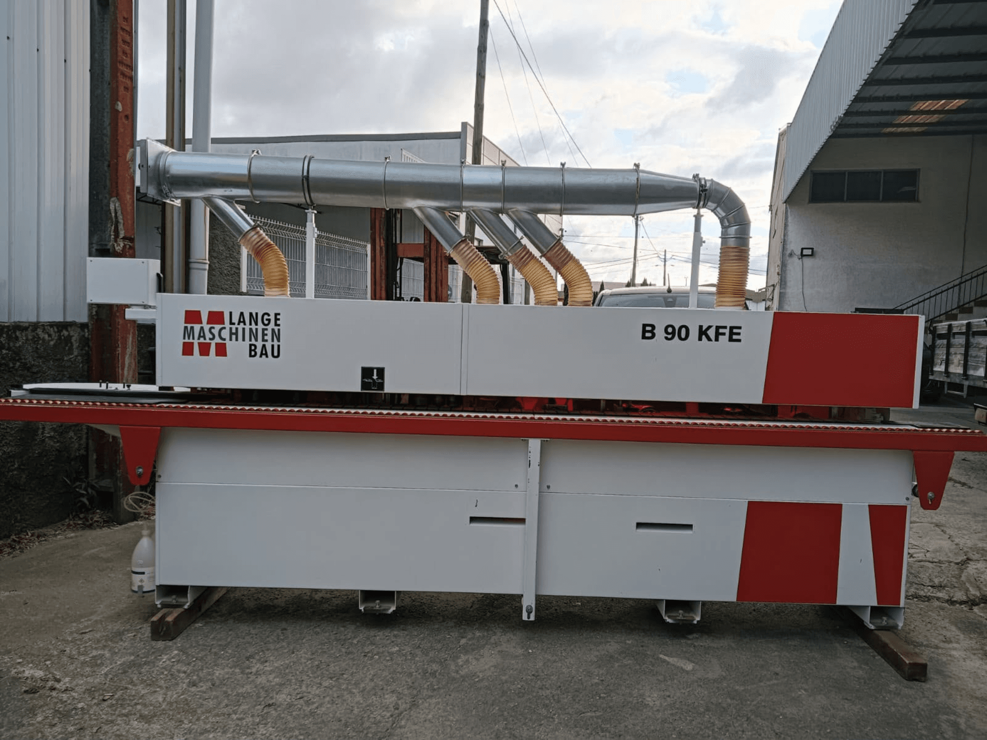 „LANGE Maschinenbau B 90 KFE“ kraštų apdirbimo staklės, matomos iš šono, su dviem išmetimo vamzdžiais ir raudonais akcentais, įrengtos pramoninėje darbo erdvėje.