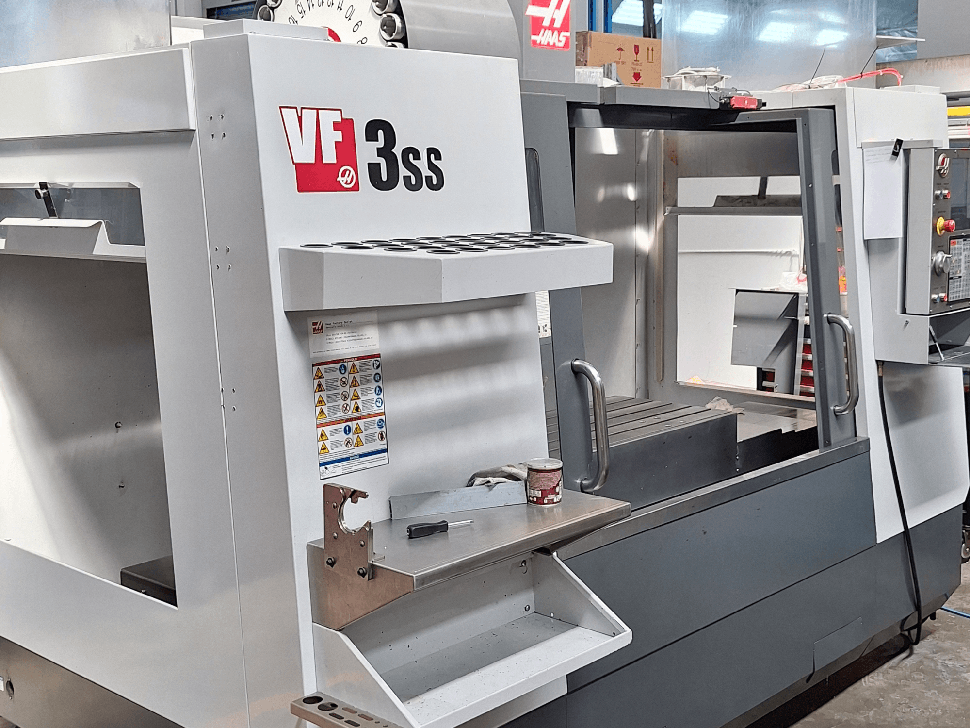 Vertikalaus apdirbimo centro "Haas VF-3SS" priekinis vaizdas, kuriame matyti valdymo skydelis, įrankių laikiklis ir darbo zona.