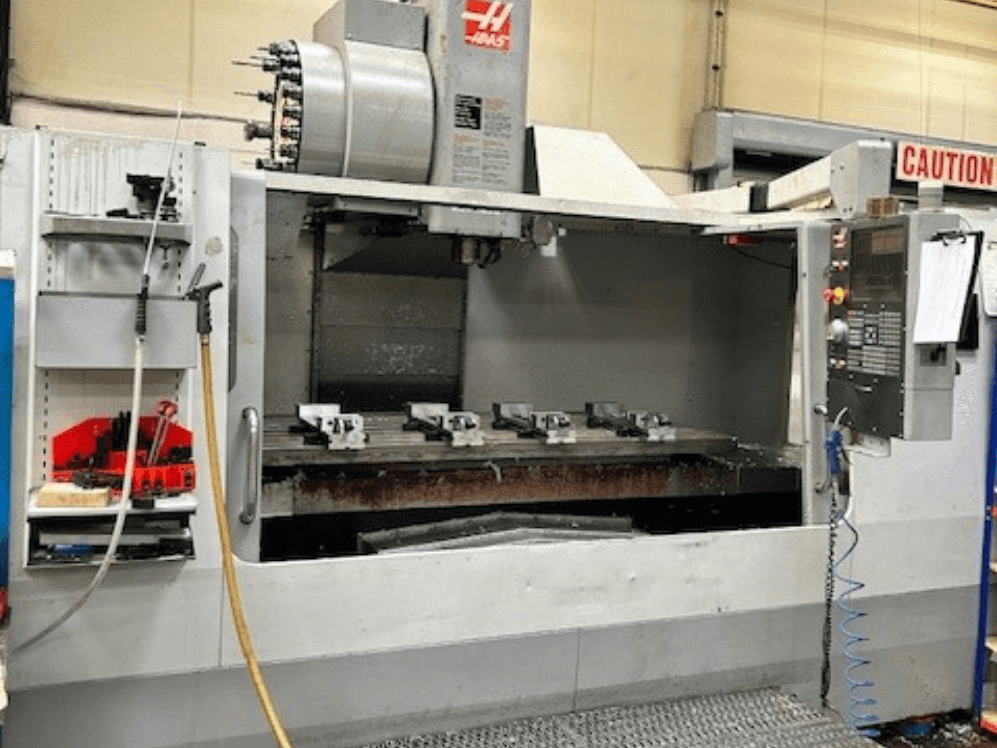 HAAS VF-9/40HE vertikalusis apdirbimo centras, vaizdas iš priekio, šone matomas įrankių laikiklis ir priedai.