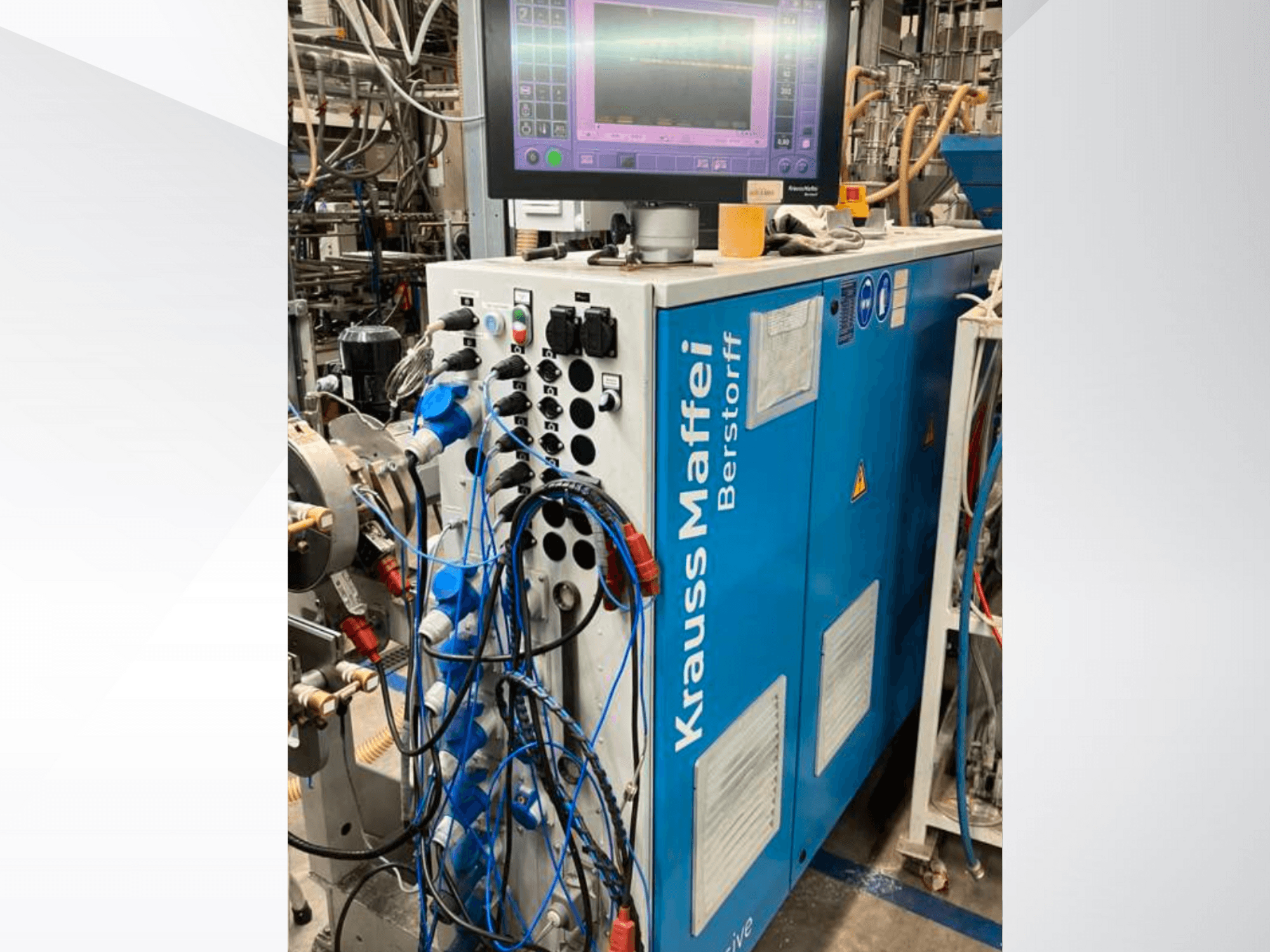 "Krauss Maffei Berstorff" pramoninė mašina su valdymo skydeliu ir monitoriumi, su įvairiais mygtukais ir prijungtomis žarnomis, vaizdas iš šono.