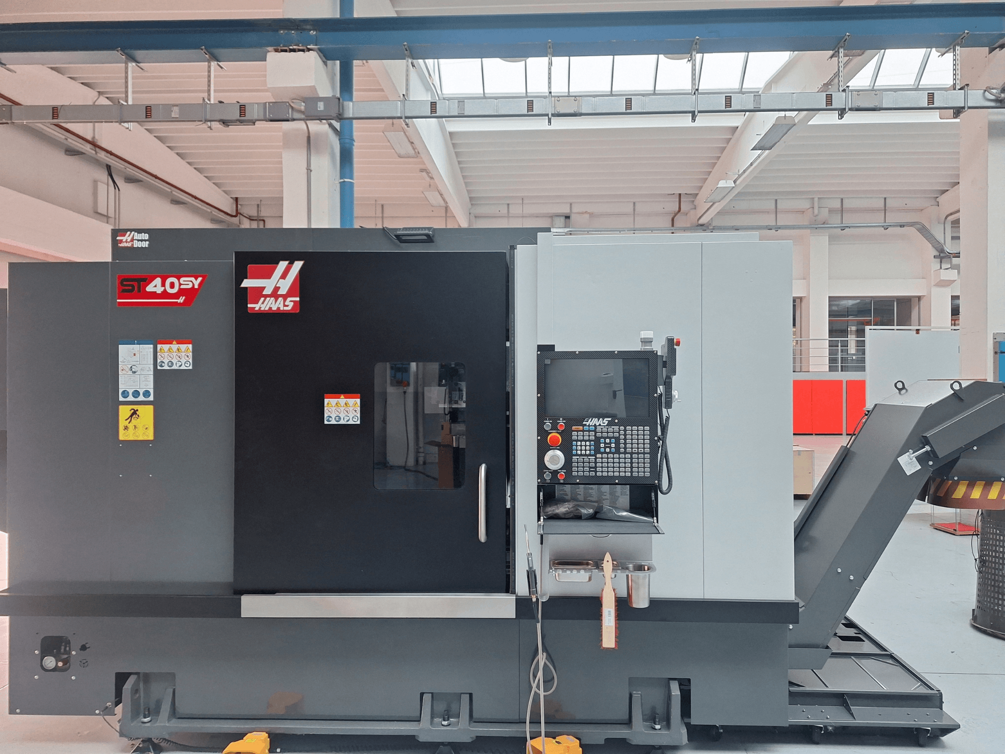 „Haas ST-40SY“ horizontalios tekinimo staklės, vaizdas iš šono, su valdymo pultu ir saugos etiketėmis.