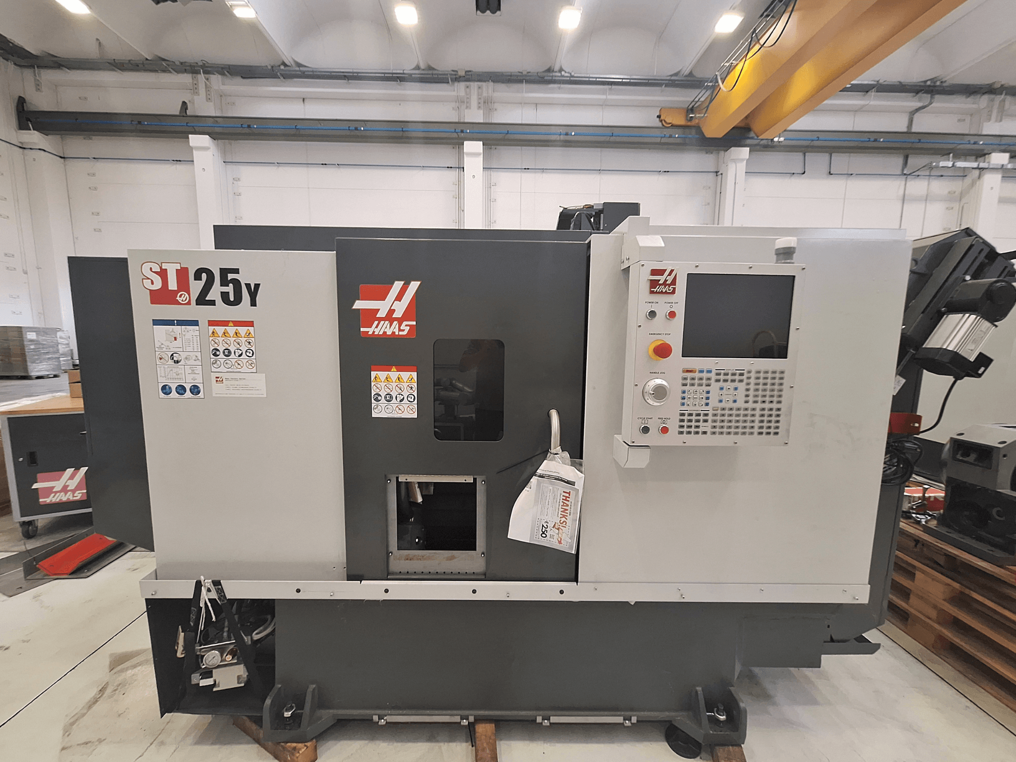 „Haas ST-25Y“ horizontalus tekinimo staklės, vaizdas iš priekio, su valdymo pultu ir saugos etiketėmis. Idealiai tinka tiksliajam apdirbimui.
