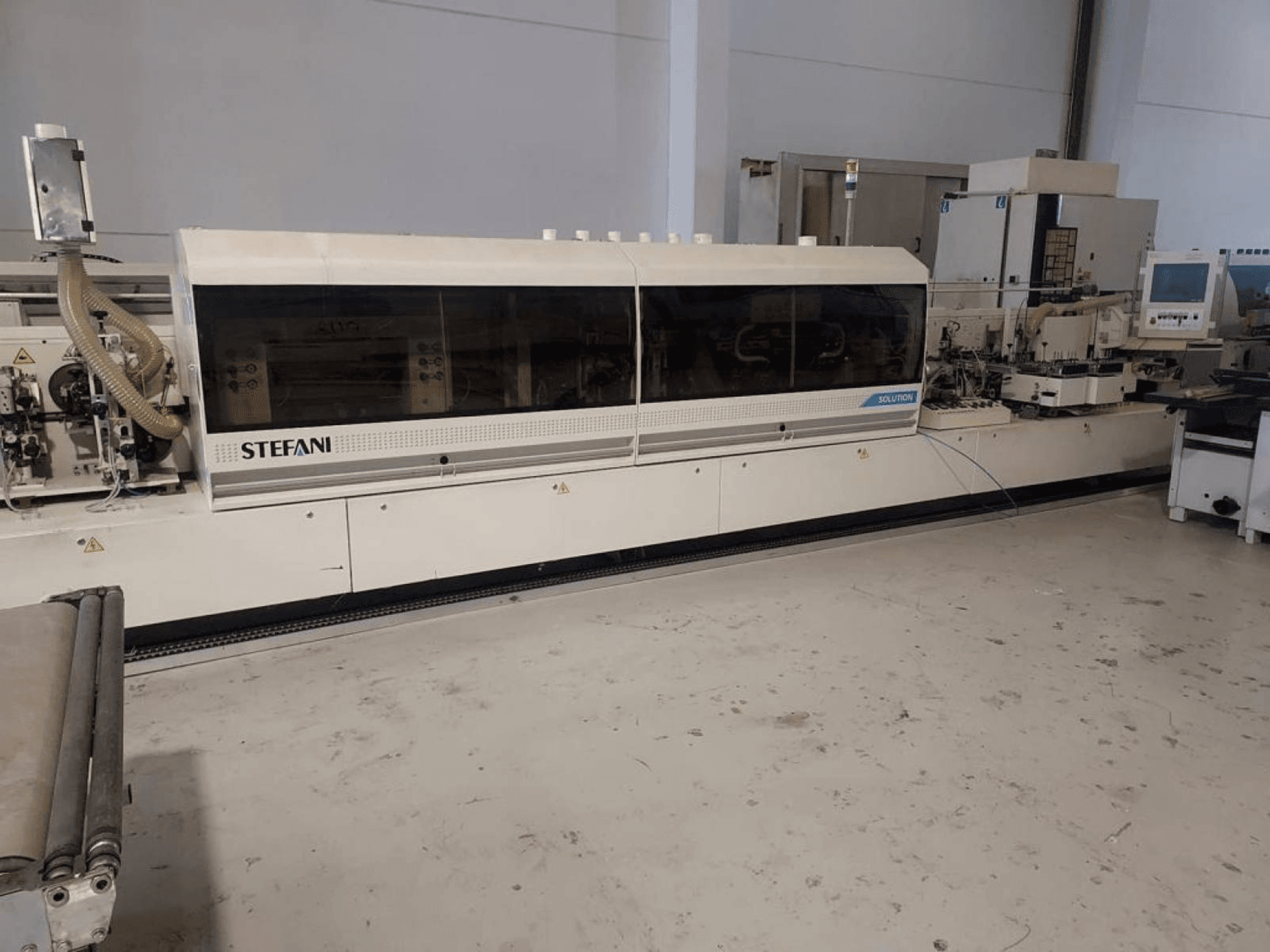 "Stefani Solutions" kraštų juostų klijavimo staklės, vaizdas iš priekio, matoma dulkių ištraukimo sistema ir valdymo skydelis, dirbtuvėse.
