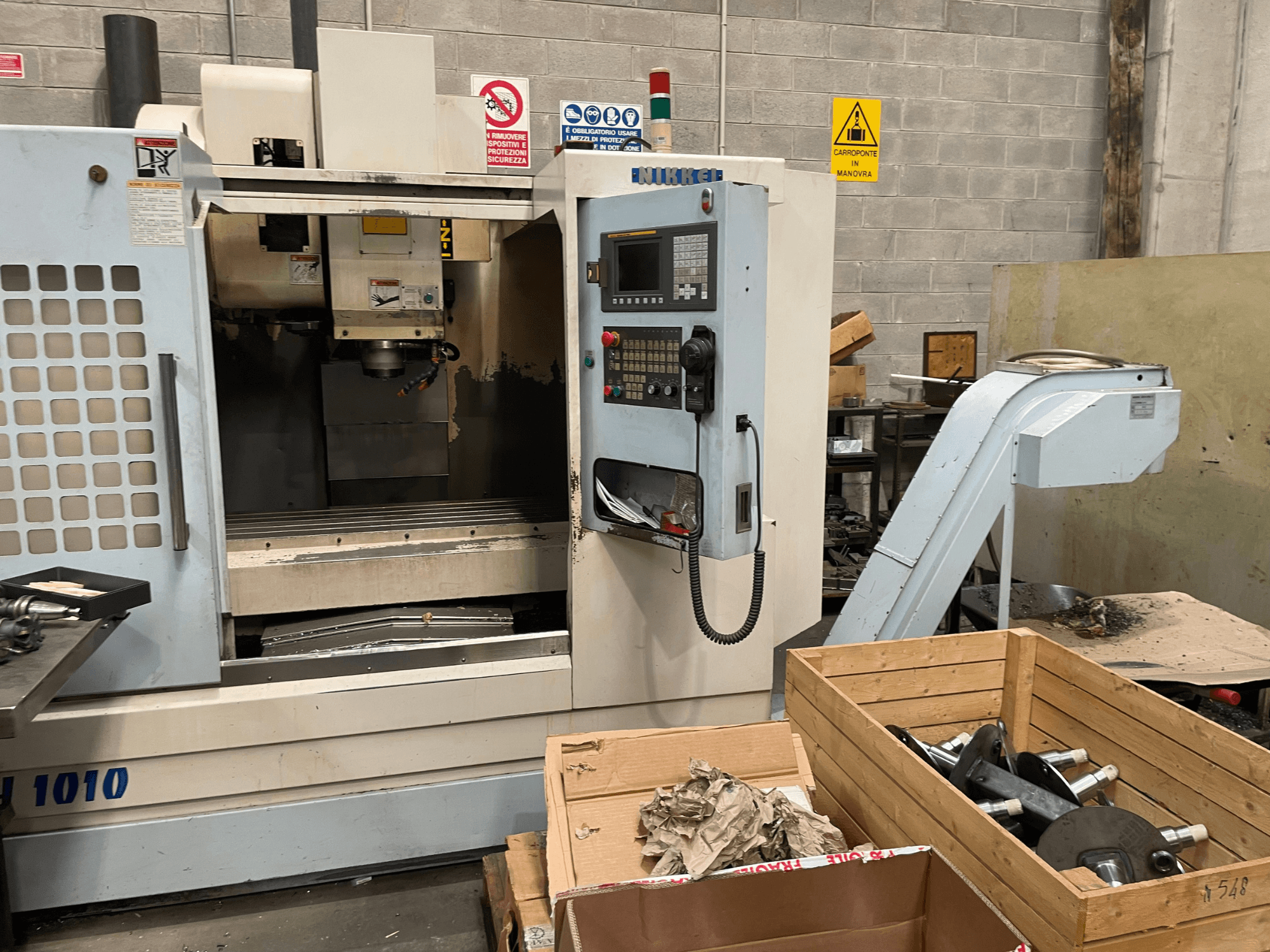 Vertikalaus apdirbimo centras Other, modelis VH-1010, žiūrint iš priekio, matomi valdymo elementai ir šalia esančios dėžės.