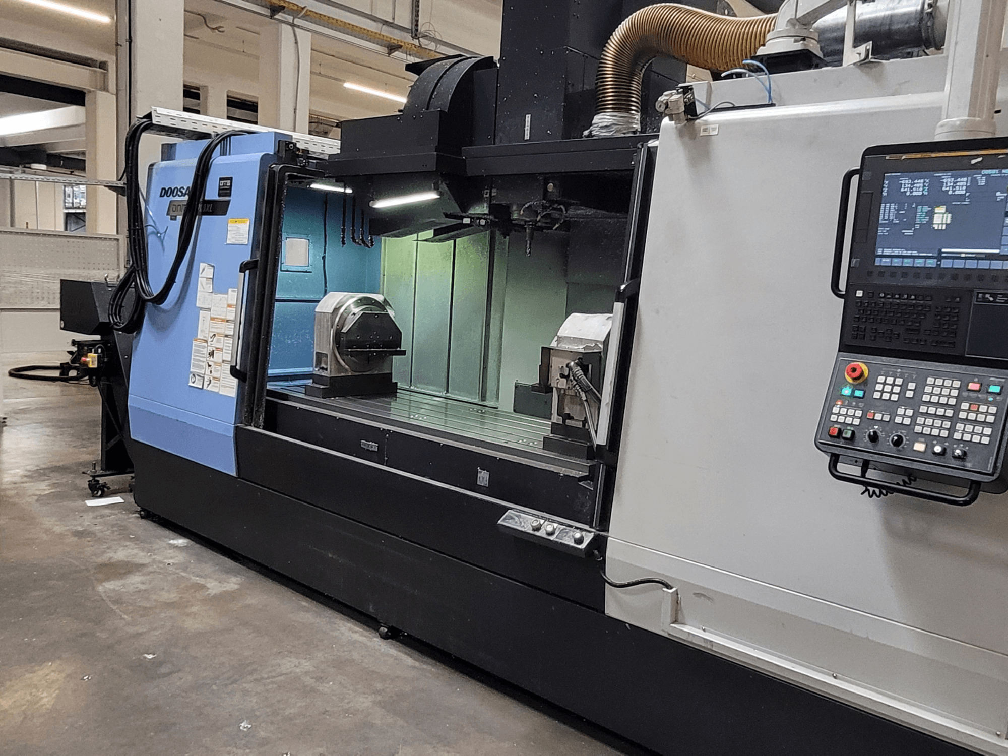 Vertikalusis apdirbimo centras „DOOSAN DNM 6700 XL“, vaizdas iš priekio, kuriame matomas valdymo pultas, darbo stalas ir apdirbimo zona.