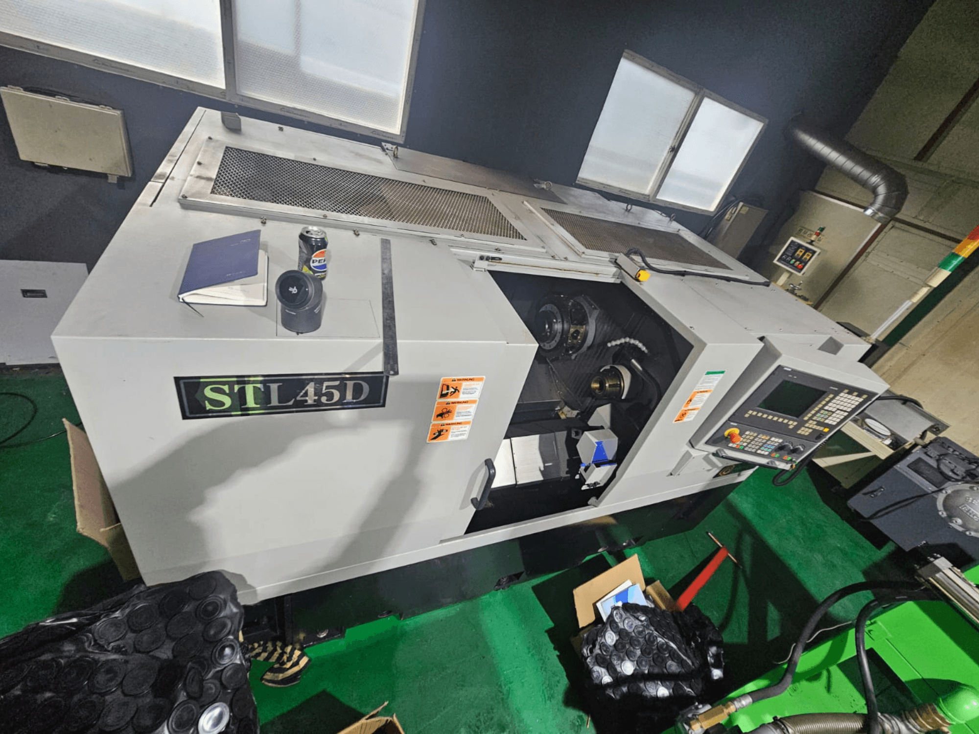 STL45D CNC staklės, žiūrint iš viršaus, matomas valdymo skydelis, cilindrinė detalė, nešiojamasis kompiuteris ir skardinė viršuje.