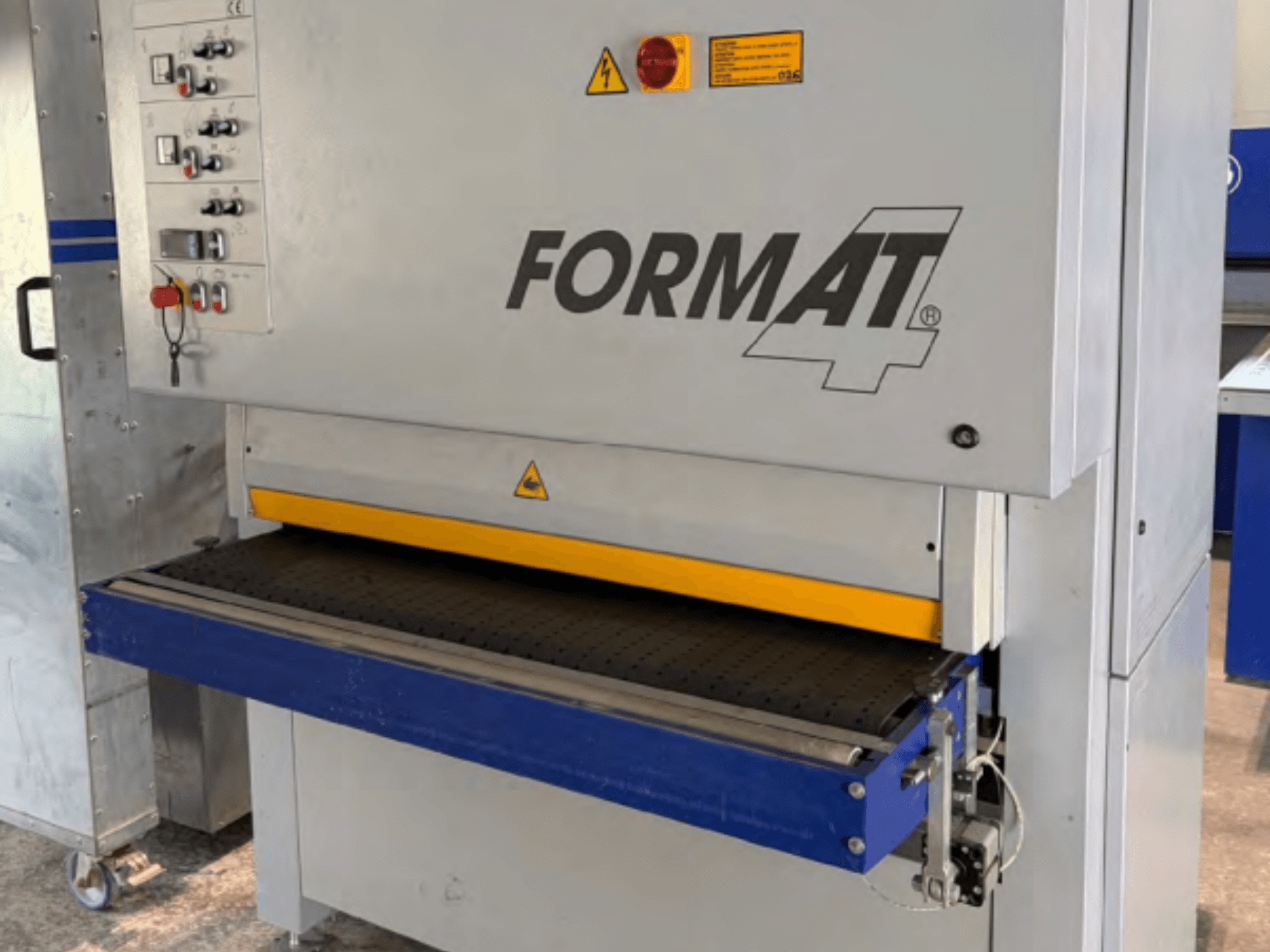 „FORMAT4 Finish 1302“ juostinis šlifuoklis, pavaizduotas iš priekio, su valdymo skydeliu, geltona šlifavimo juosta ir mėlynu konvejeriniu stalu.