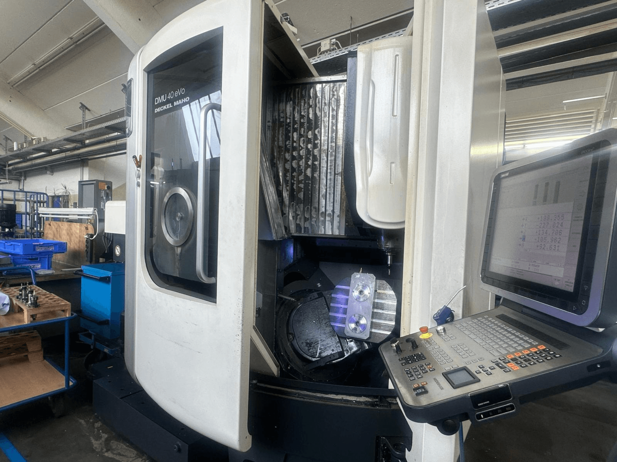 "Deckel Maho" frezavimo staklės DMU 40 eVo dirbtuvėse, vaizdas iš priekio, matomas valdymo skydelis ir metalinė detalė verpstėje.