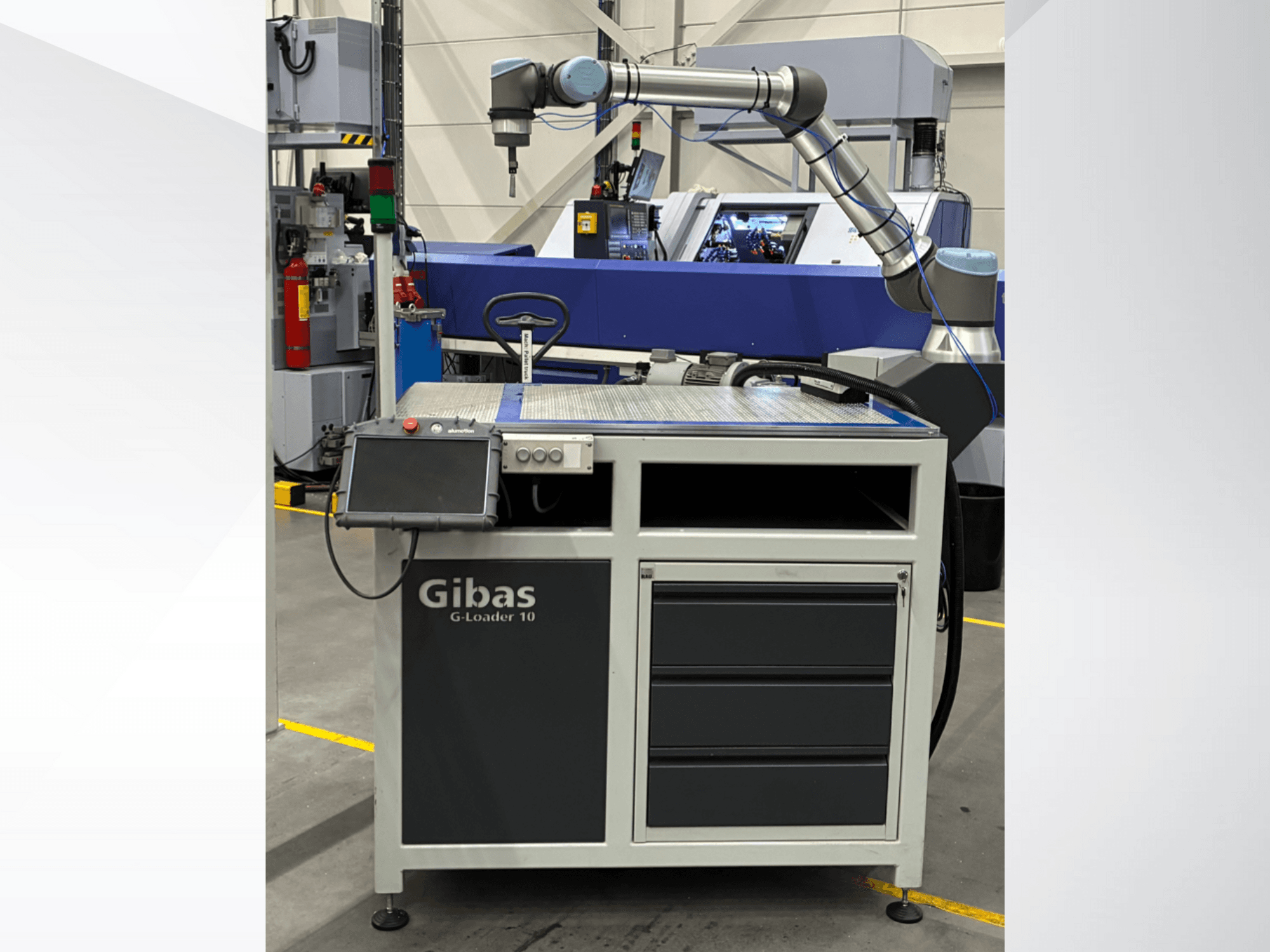 "Gibas G-Loader 10" su roboto ranka, vaizdas iš priekio; jutiklinio ekrano valdymas ir stalčių laikymas pramoninėje aplinkoje.