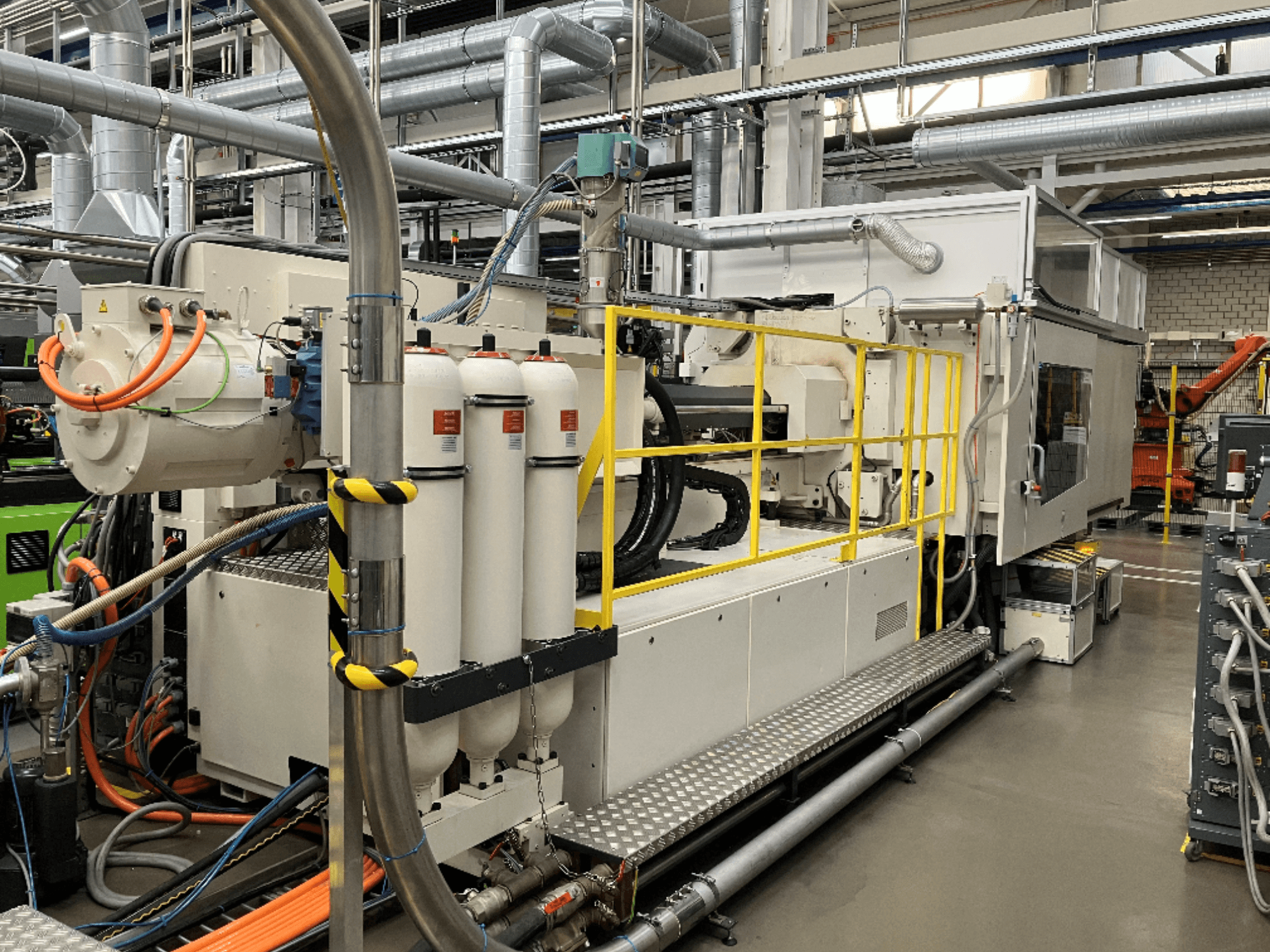 Pramoninė mašina su baltu ir pilku korpusu, keliomis žarnomis ir filtravimo talpyklomis; šoninis vaizdas, rodantis darbinę sąrangą.