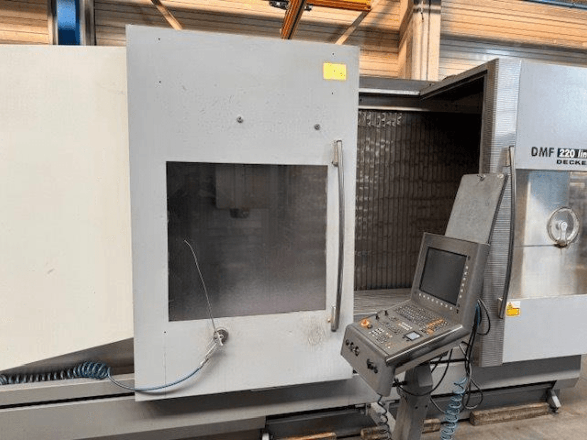 DECKEL MAHO DMF 220 linijinio vertikaliojo apdirbimo centro priekinis vaizdas, kuriame matyti valdymo skydelis ir atidarytos staklių durys.