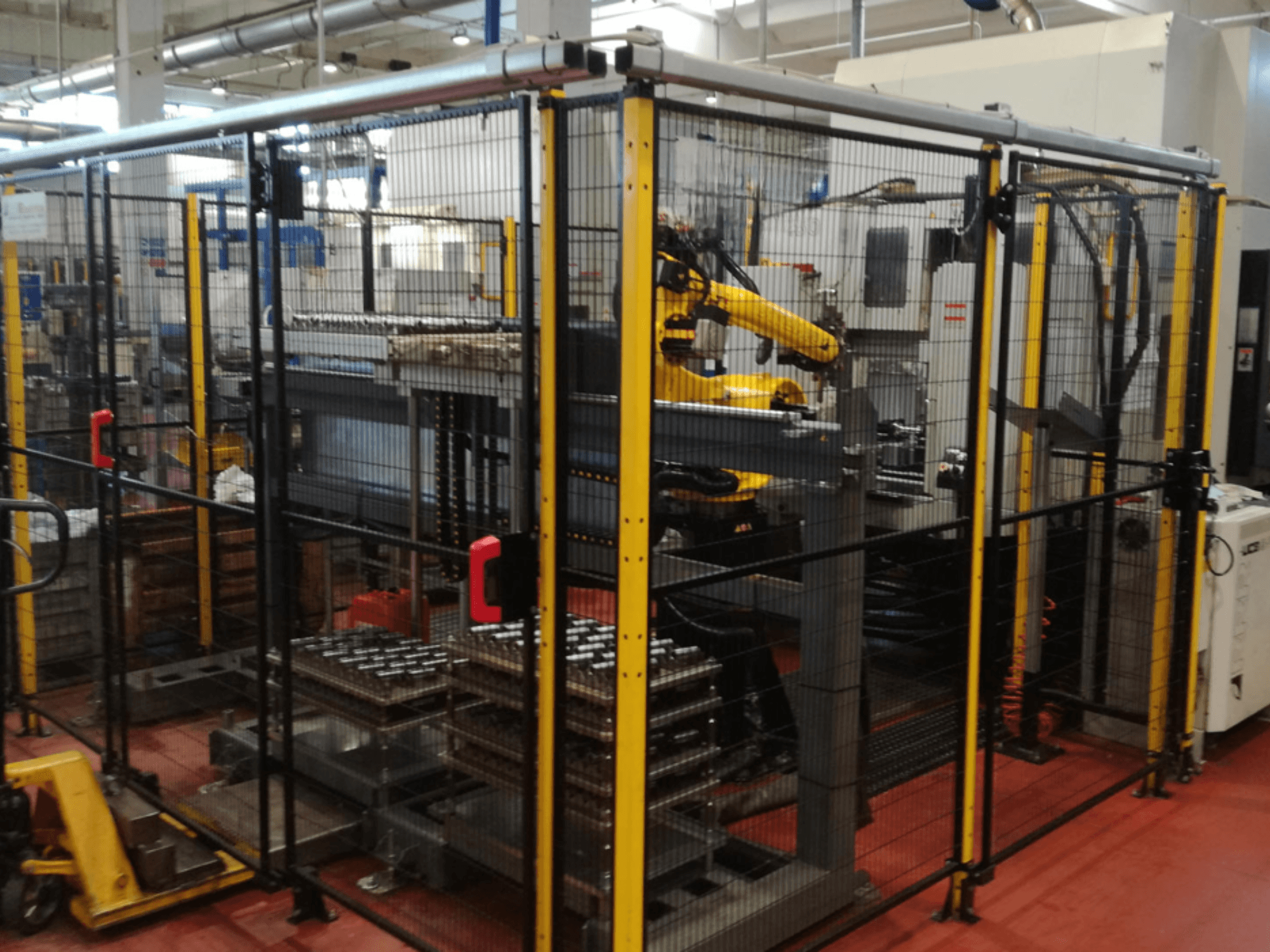 Vertikalus apdirbimo centras "Enshu EV450" aptvertoje darbo erdvėje, kurioje yra roboto rankos ir kelios viena ant kitos sukrautos detalės. Vaizdas iš priekio.