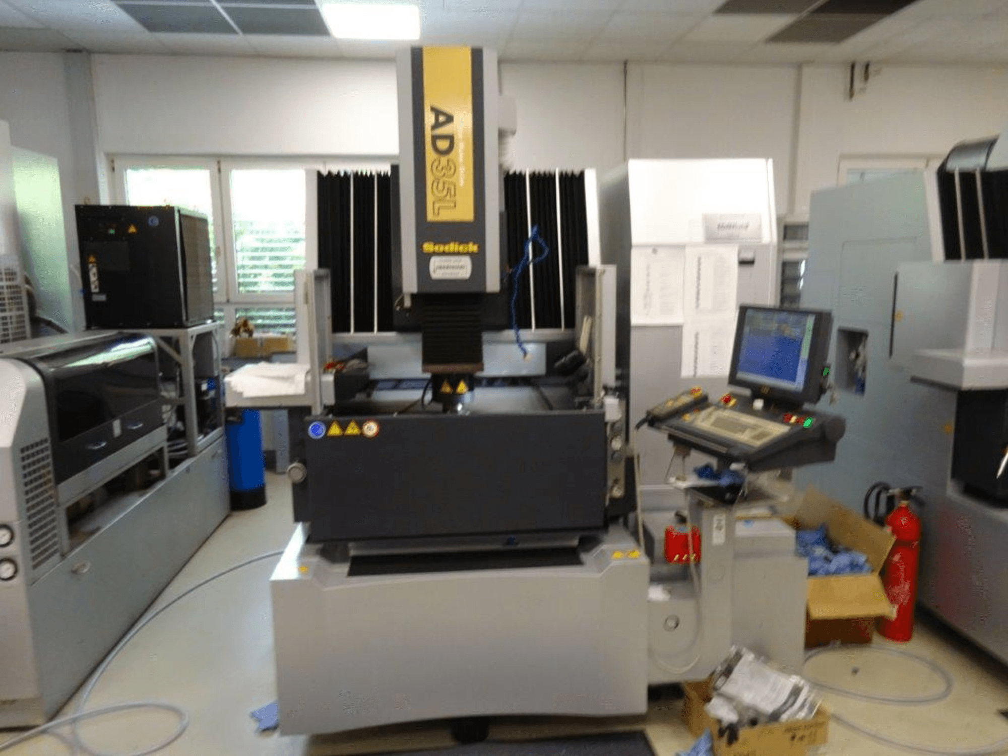 Sodick AD35L CNC staklės iš priekio, su valdymo skydeliu, aušinimo įrenginiu ir saugos indikatoriais.