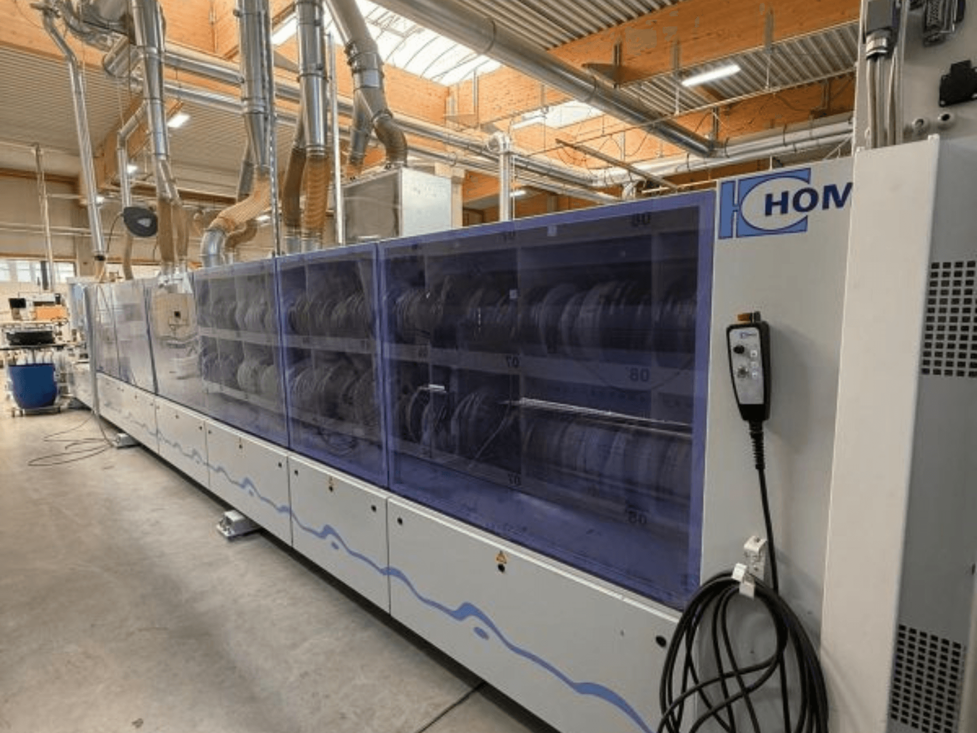 Pramoninė skalbimo mašina HOM, vaizdas iš priekio, su permatomu skydeliu, kuriame rodomi indai; valdymo skydelis su mygtukais šone.