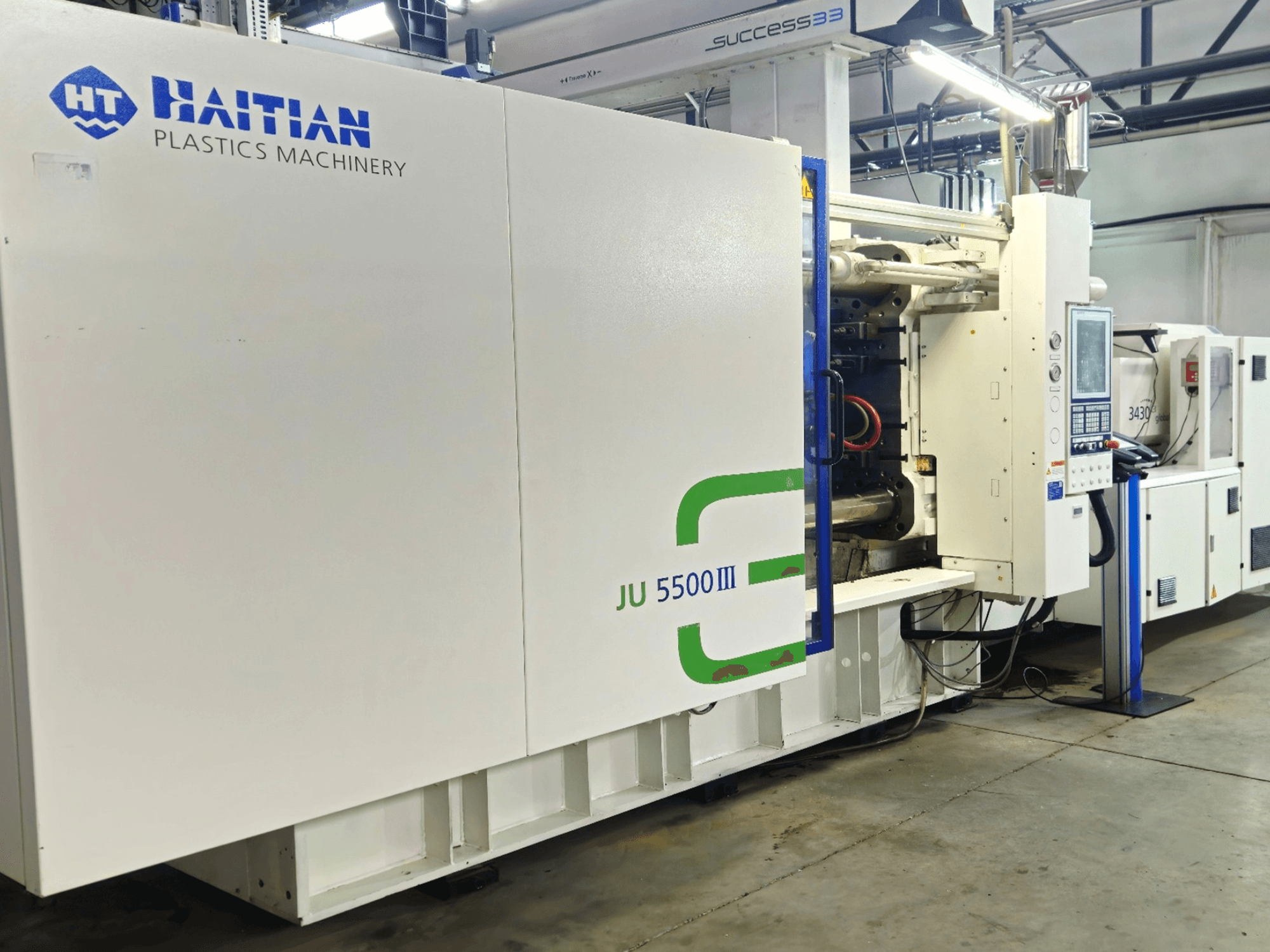 Haičio JU 5500III plastiko mašinos gamykloje, iš priekio matomas valdymo skydelis ir gamybos zona.