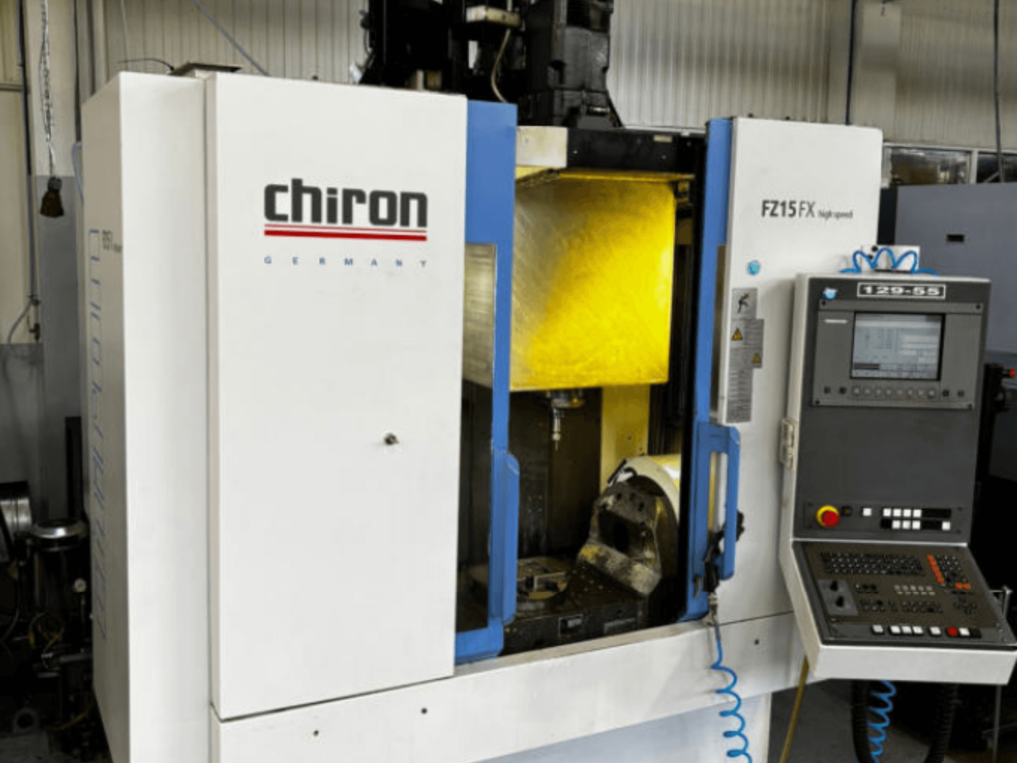 Vertikalus apdirbimo centras „CHIRON FZ 15FX“, vaizdas iš priekio, kuriame matomas valdymo pultas ir apdirbimo zona su įrankiais.