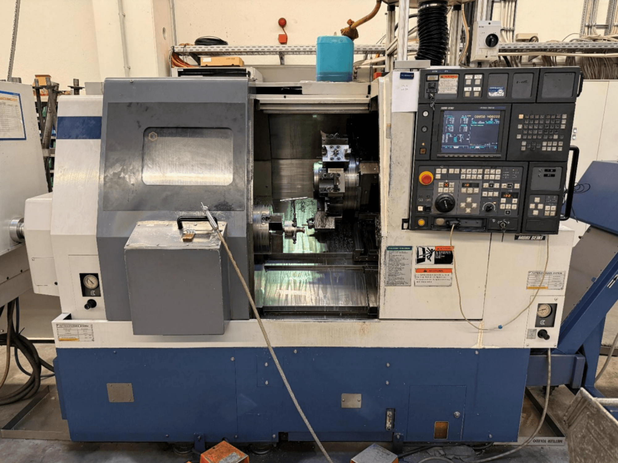 MORI SEIKI SL-250ASMC tekinimo-frezavimo centras, vaizdas iš priekio, kuriame matomas valdymo pultas ir veikiantis ruošinio griebtuvas.