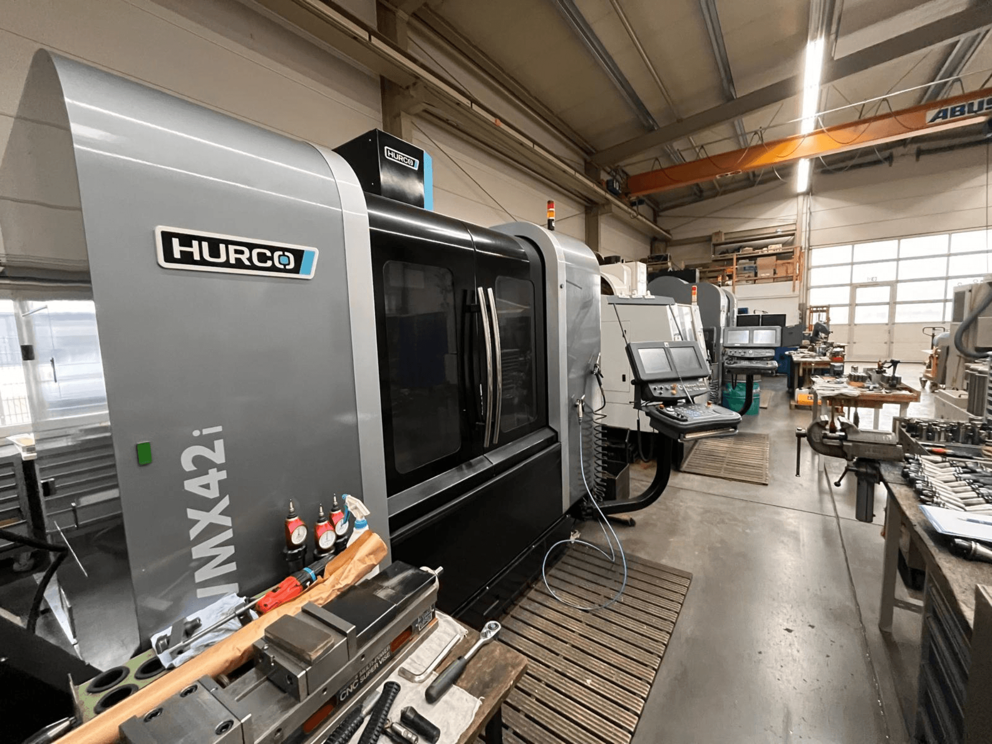 Hurco VMX42i CNC staklės dirbtuvėse, vaizdas iš priekio. Valdymo skydelis, pilkas korpusas ir pramoninė aplinka.