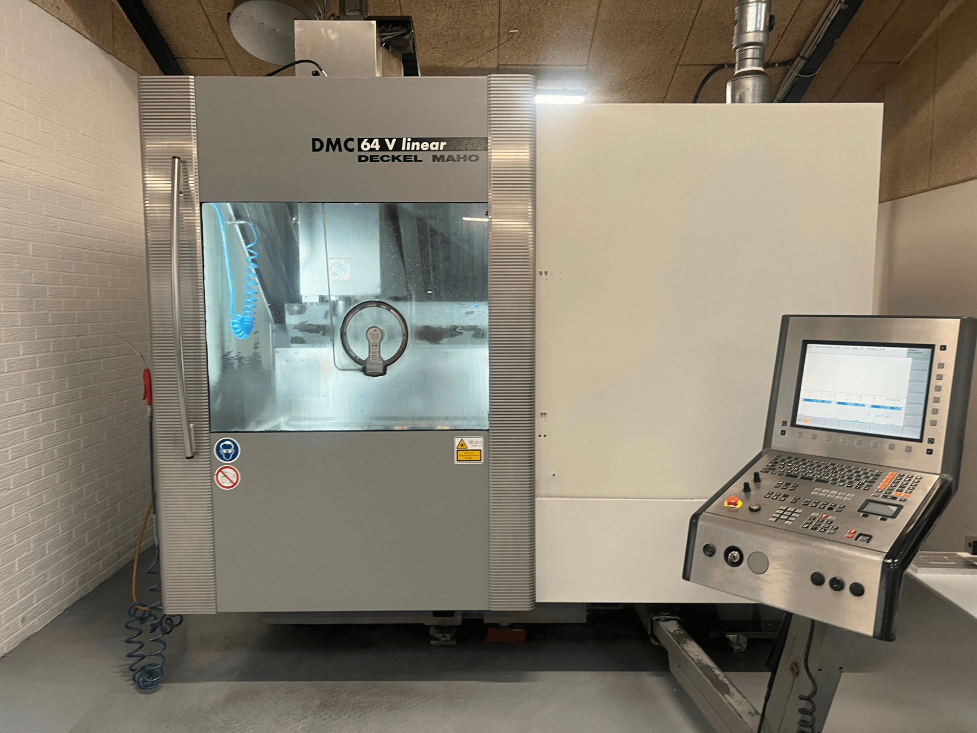 "Deckel Maho" DMC 64 V Linear, CNC apdirbimo centro vaizdas iš priekio, matomas valdymo skydelis ir aušinimo skysčio purkštukas.