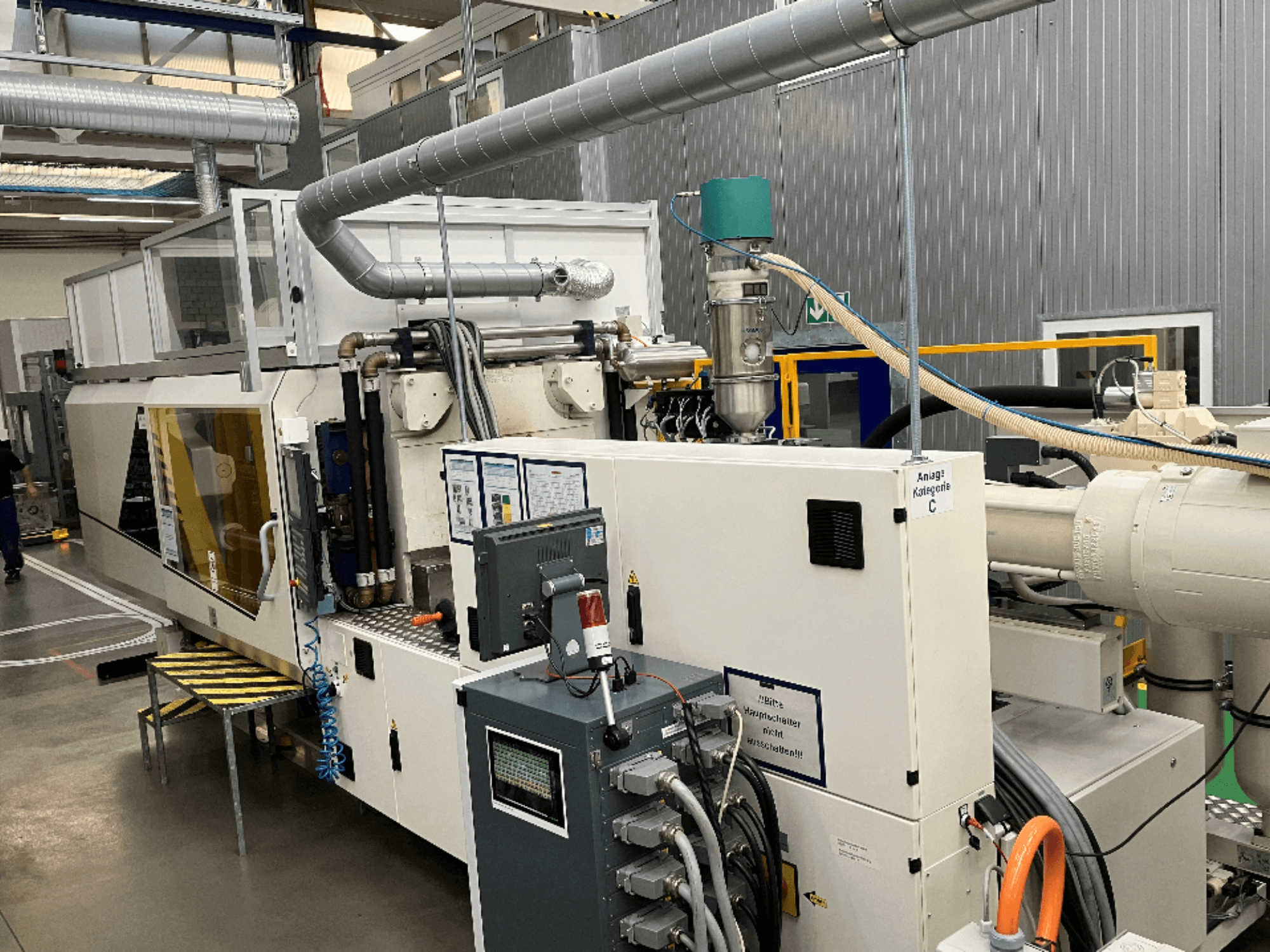 Švirkštinio liejimo mašinos vaizdas iš priekio su prekės ženklo etikete, valdymo skydeliu ir matomomis žarnomis gamykloje.