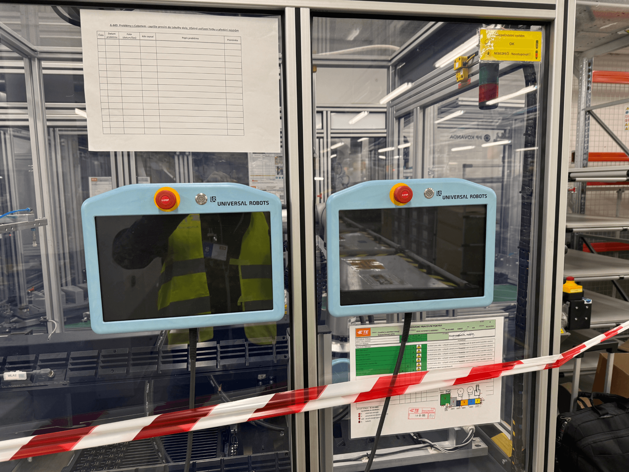 "Universal Robots UR5 e" roboto rankos valdymo skydelis su dviem monitoriais, avarinio stabdymo mygtukais ir saugos instrukcijomis.