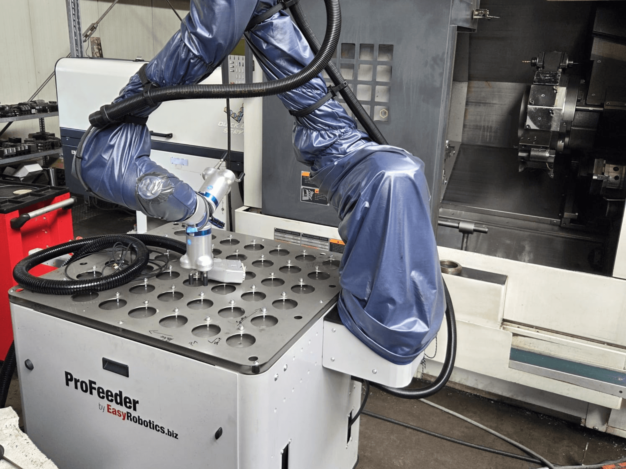 Bendradarbiavimo robotas EASYROBOTICS ProFeeder iš priekio, kai roboto ranka uždėta ant perforuoto metalinio stalo.
