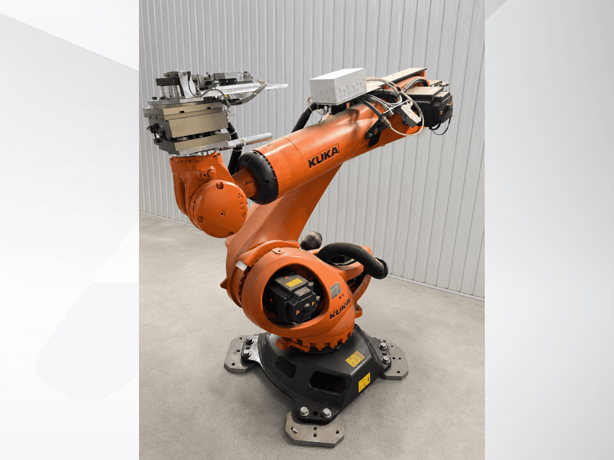 Papildoma „KUKA KR 90 R3100“ roboto ranka oranžinės spalvos, vaizdas iš šono, kuriame matomi sąnariai, valdiklis ir ant galinio veikiklio pritvirtintas įrankis.