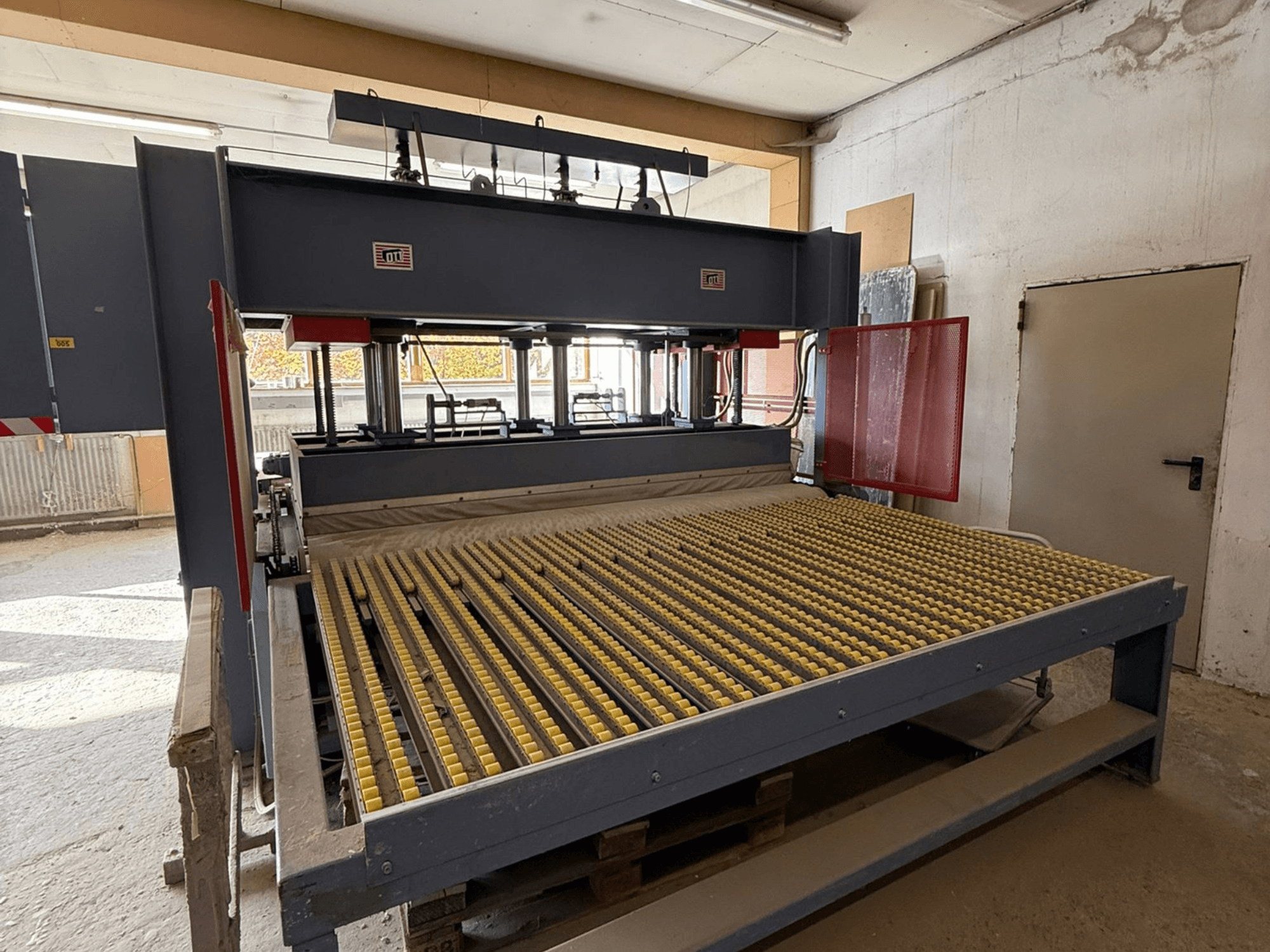 Pramoninė mašina su geltonais ritinėliais, vaizdas iš priekio, matomas prekės ženklo logotipas, naudojama medžiagoms apdoroti dirbtuvėse.