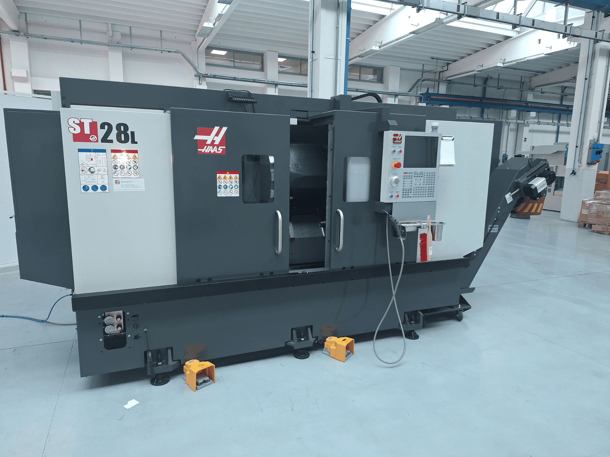 Haas ST-28L horizontalaus tekinimo staklių vaizdas iš šono, kuriame matomas valdymo skydas, valdymo mygtukai ir saugos etiketės.
