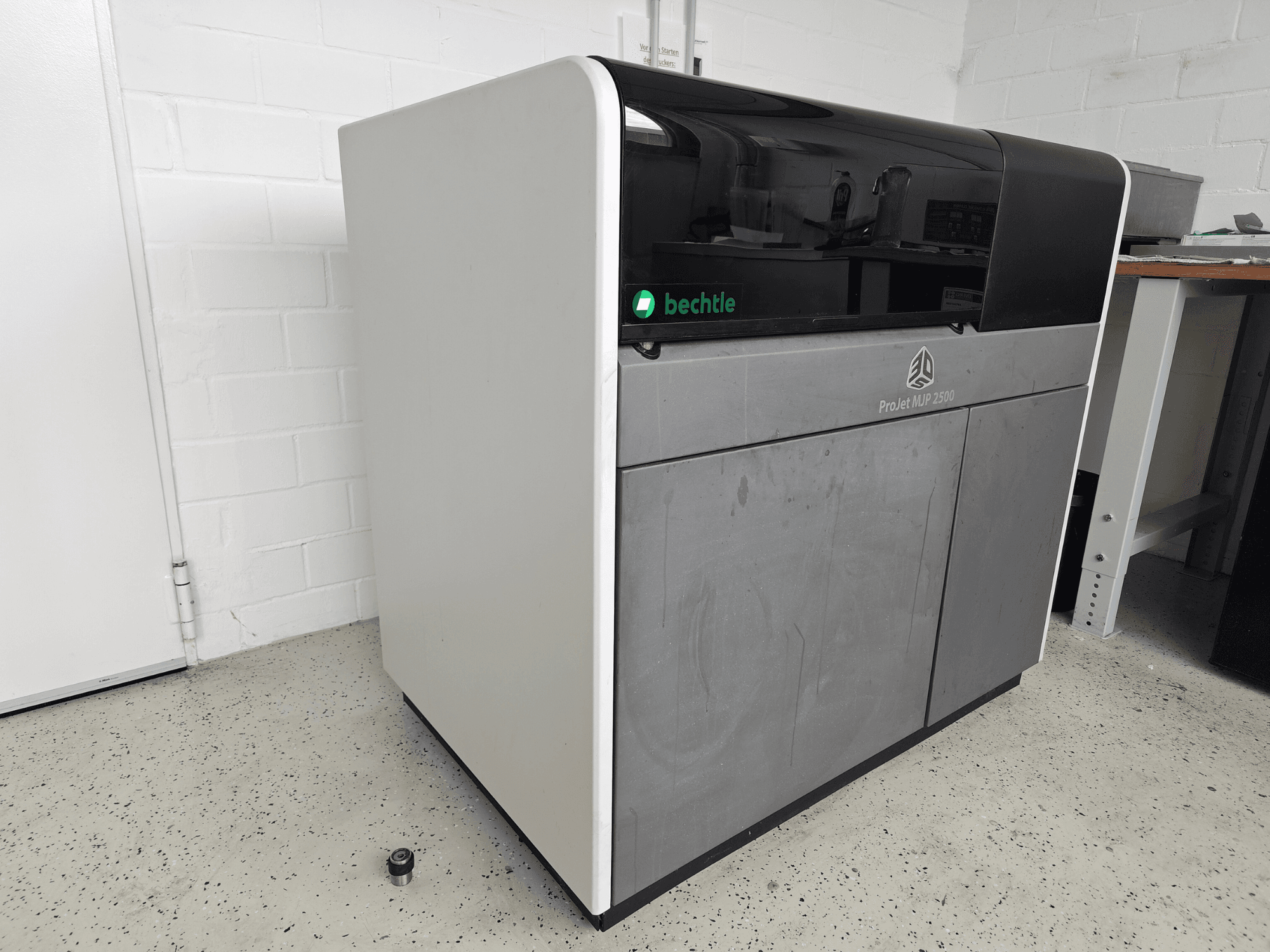 „3D Systems ProJet MJP 2500 Plus“ plastiko spausdintuvas, vaizdas iš priekio; išsiskiria elegantišku dizainu su tamsiu viršumi ir šviesiu korpusu.