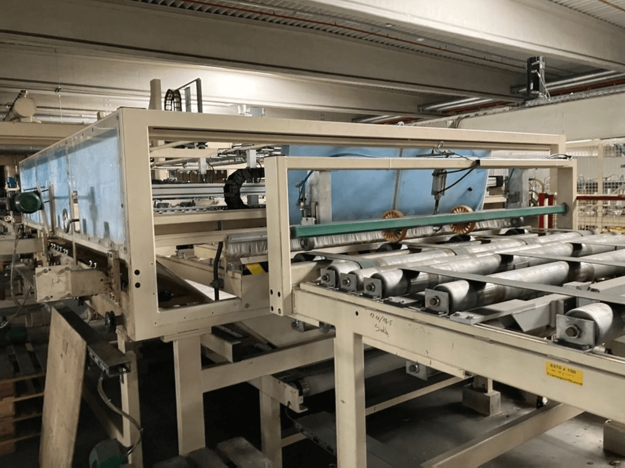 WEMHÖNER KT-F-1E laminavimo presas, vaizdas iš šono, su ritinėliais ir valdikliais medžiagoms apdoroti gamykloje.