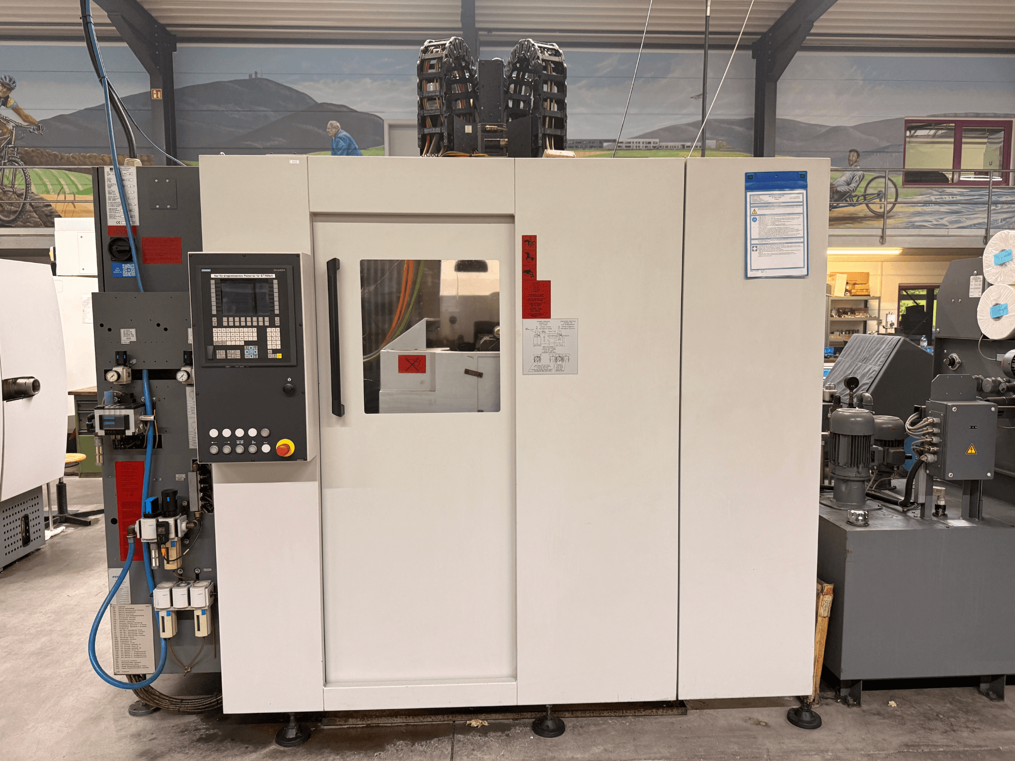 Baltas CNC apdirbimo centras su valdymo skydeliu, vaizdas iš priekio, su mygtukais ir skaitmeniniu ekranu, dirbtuvėse.