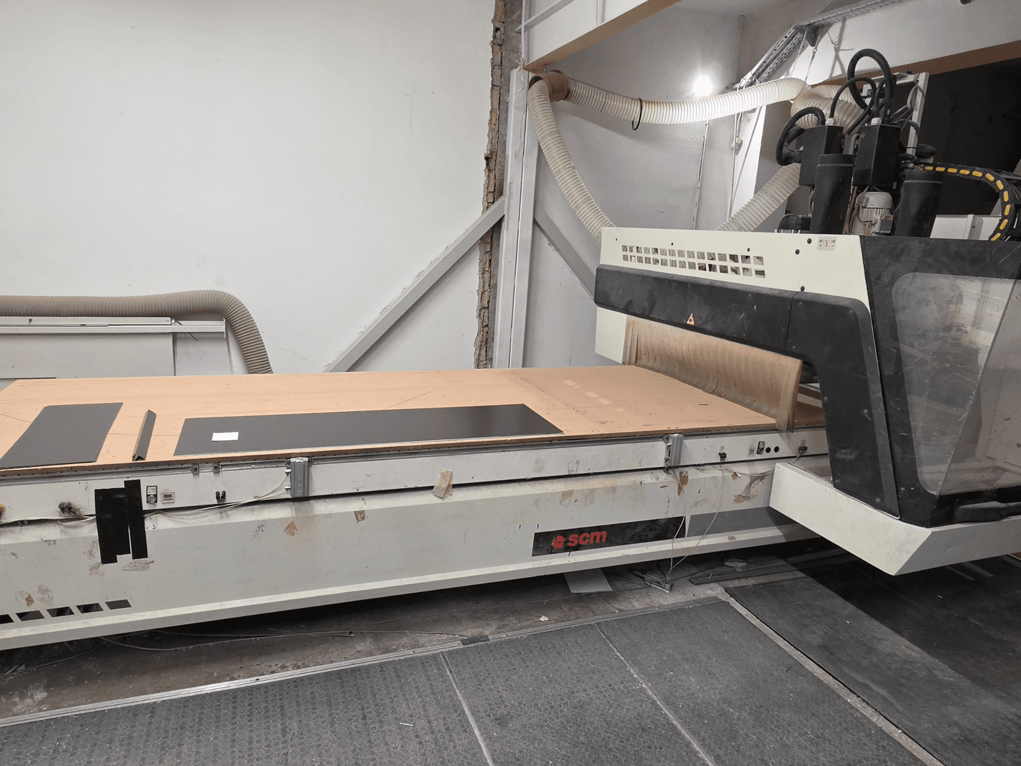 SCM RECORD 132 CNC medžio apdirbimo centras, vaizdas iš šono: matomas plokščias darbo stalas su juodais ruošiniais ir dulkių surinkimo sistema.