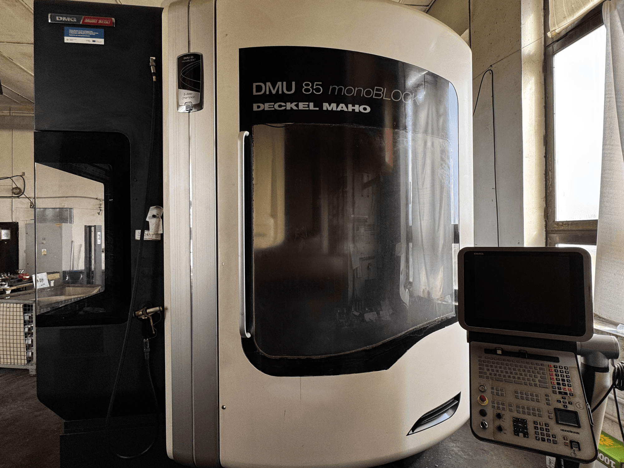 DMG MORI DMU 85 monoBLOCK vertikalusis apdirbimo centras, vaizdas iš priekio su valdymo skydeliu ir dideliu stebėjimo langu.