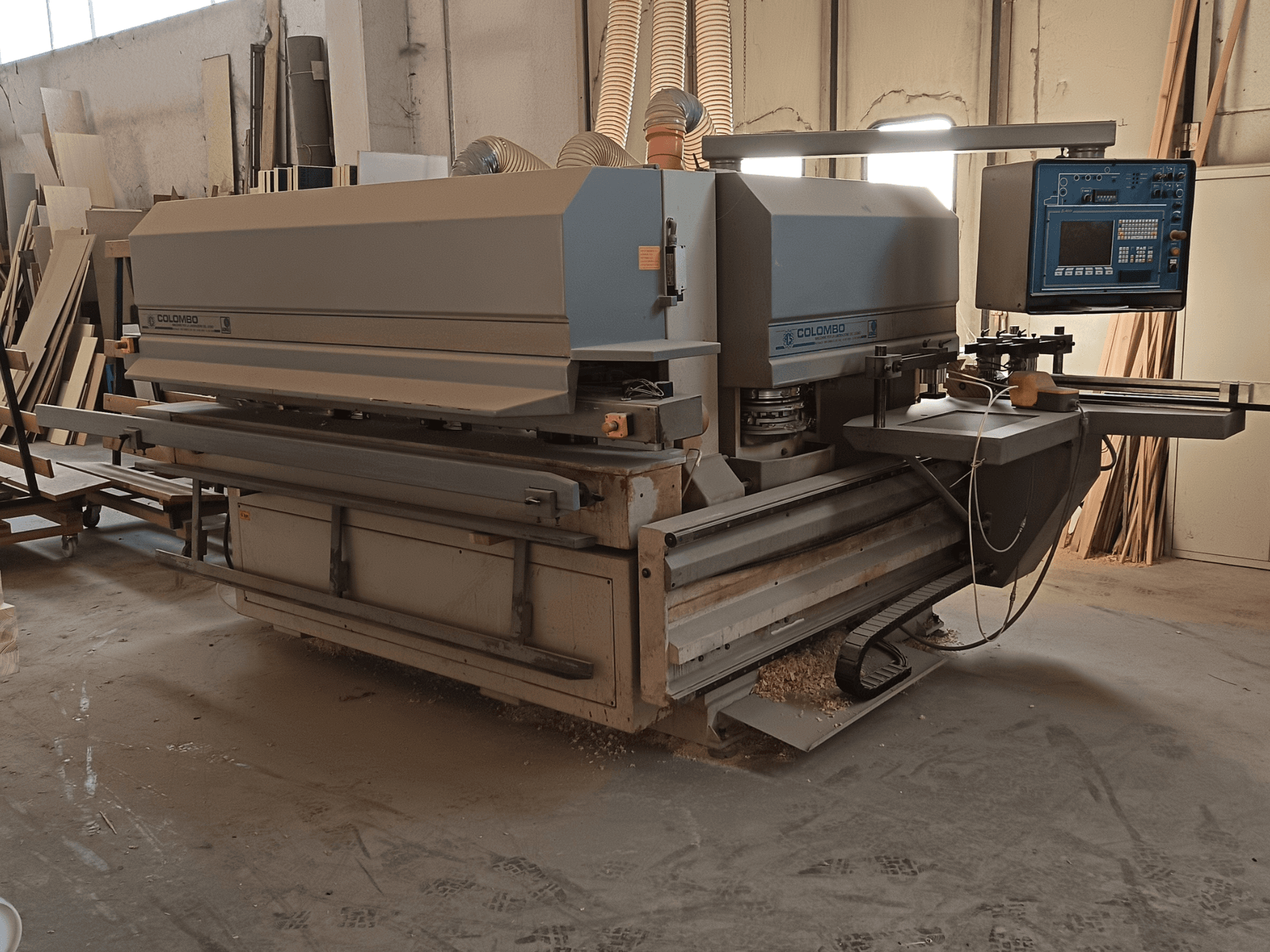 Colombo medžio apdirbimo staklės, šoninis vaizdas, kuriame matomas valdymo skydelis, pjovimo peiliai ir pjūklo dulkių sankaupos dirbtuvėse.