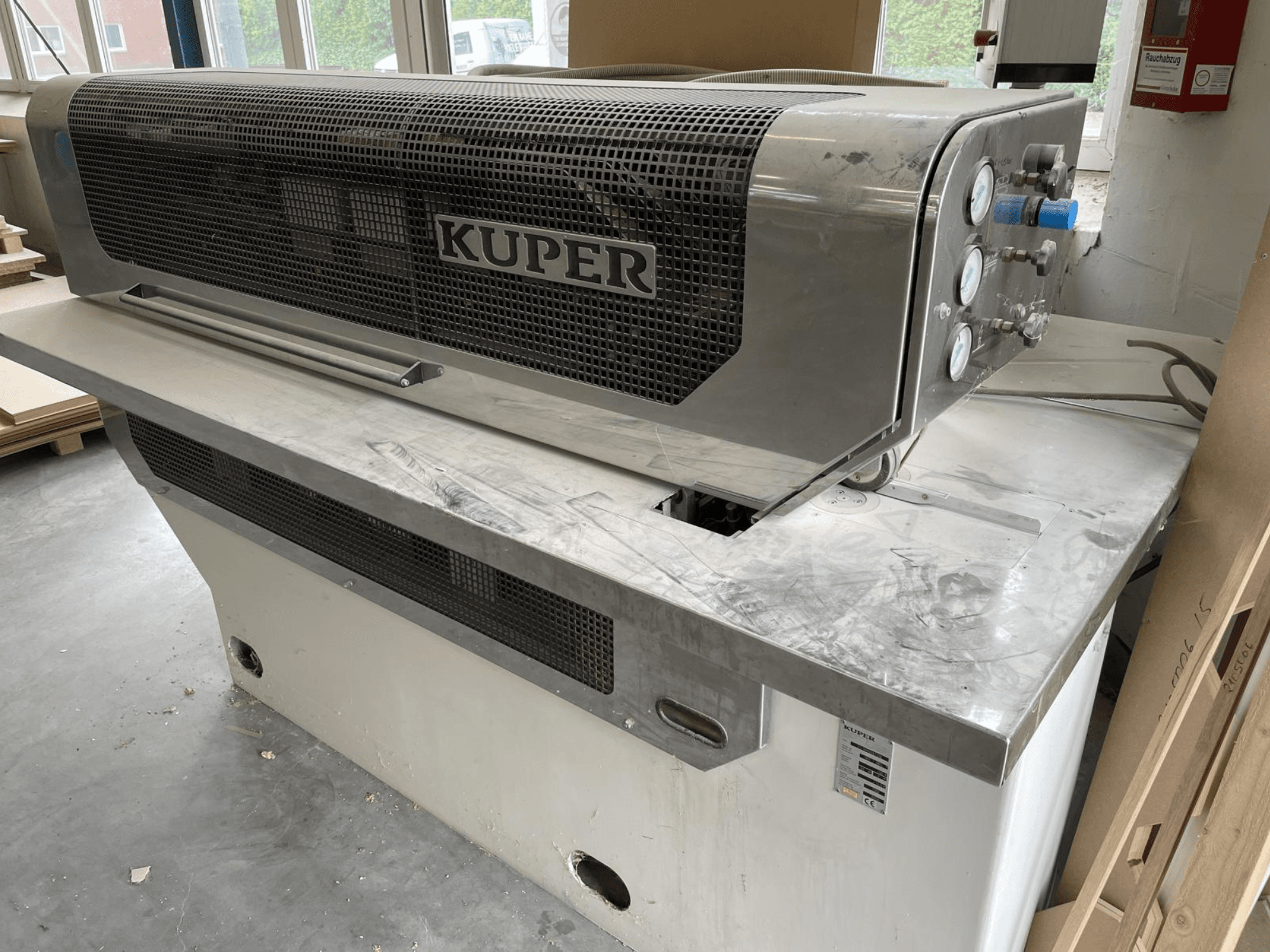 Faneros giljotina KUPER FLI, vaizdas iš priekio, su nerūdijančio plieno korpusu, matuokliais ir švaria pjovimo zona ant darbo stalo.