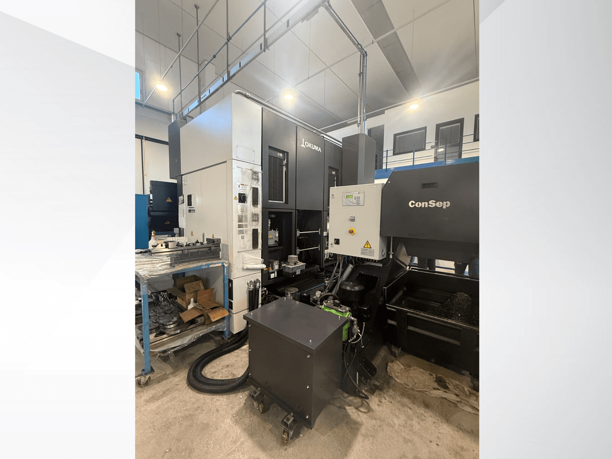 "Okuma" apdirbimo centras su "ConSep" įrenginiu, vaizdas iš šono, rodomi valdikliai ir pramoninė sąranka, įskaitant metalo drožlių talpyklą.