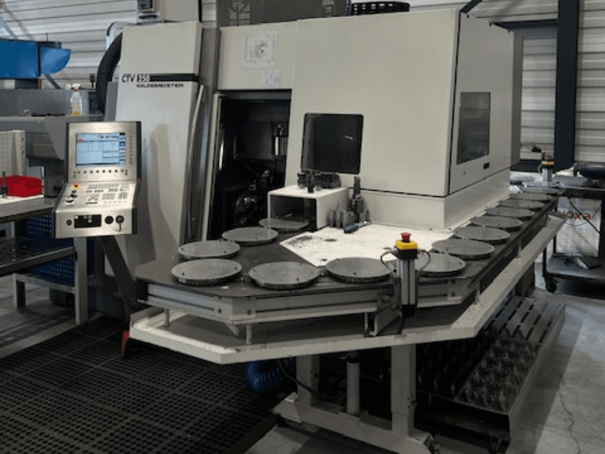 Alt tekstas: CTV E33 "Goldmeister" apdirbimo įrenginys dirbtuvėse, vaizdas iš priekio, su valdymo pultu ir keliomis apskritomis darbo platformomis.