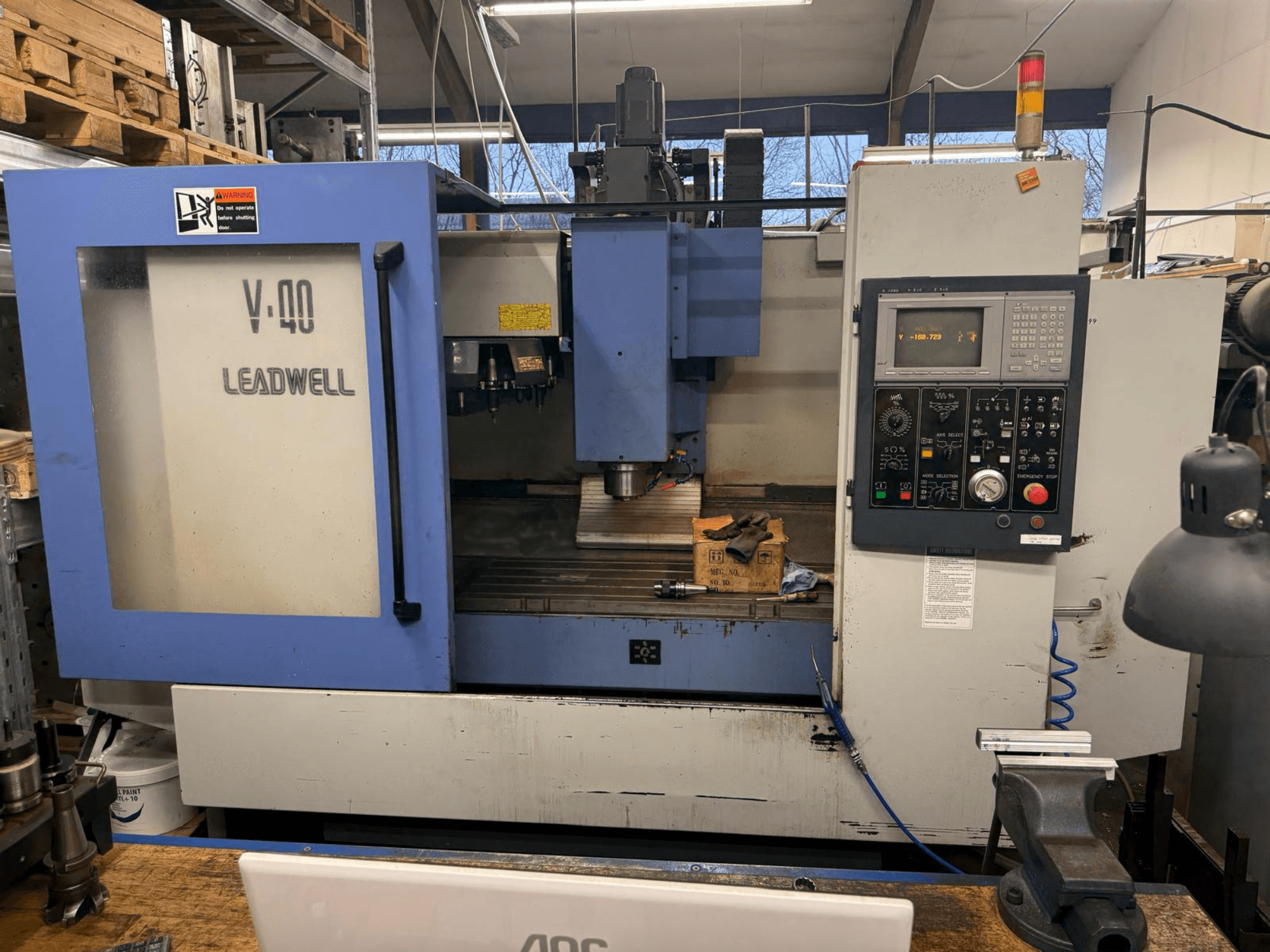 LEADWELL V-40 CNC frezavimo staklės, vaizdas iš priekio: valdymo skydelis, pjovimo įrankiai ir įtvaras ant darbo stalo.
