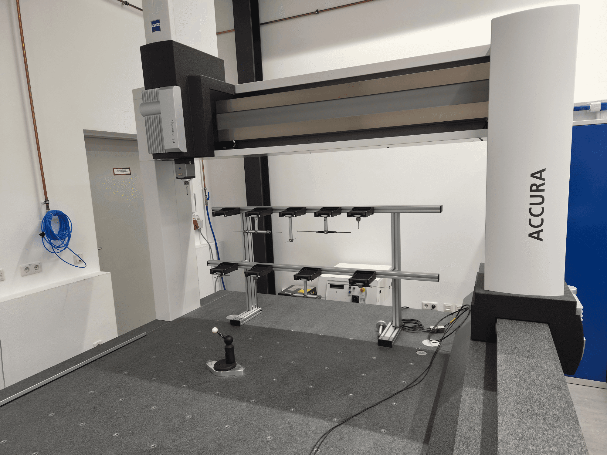 ZEISS ACCURA 16/24/10 CMM vaizdas iš priekio, kuriame matyti matavimo ranka, pagrindas ir valdymo sąsaja ant pilkos spalvos kiliminės dangos.
