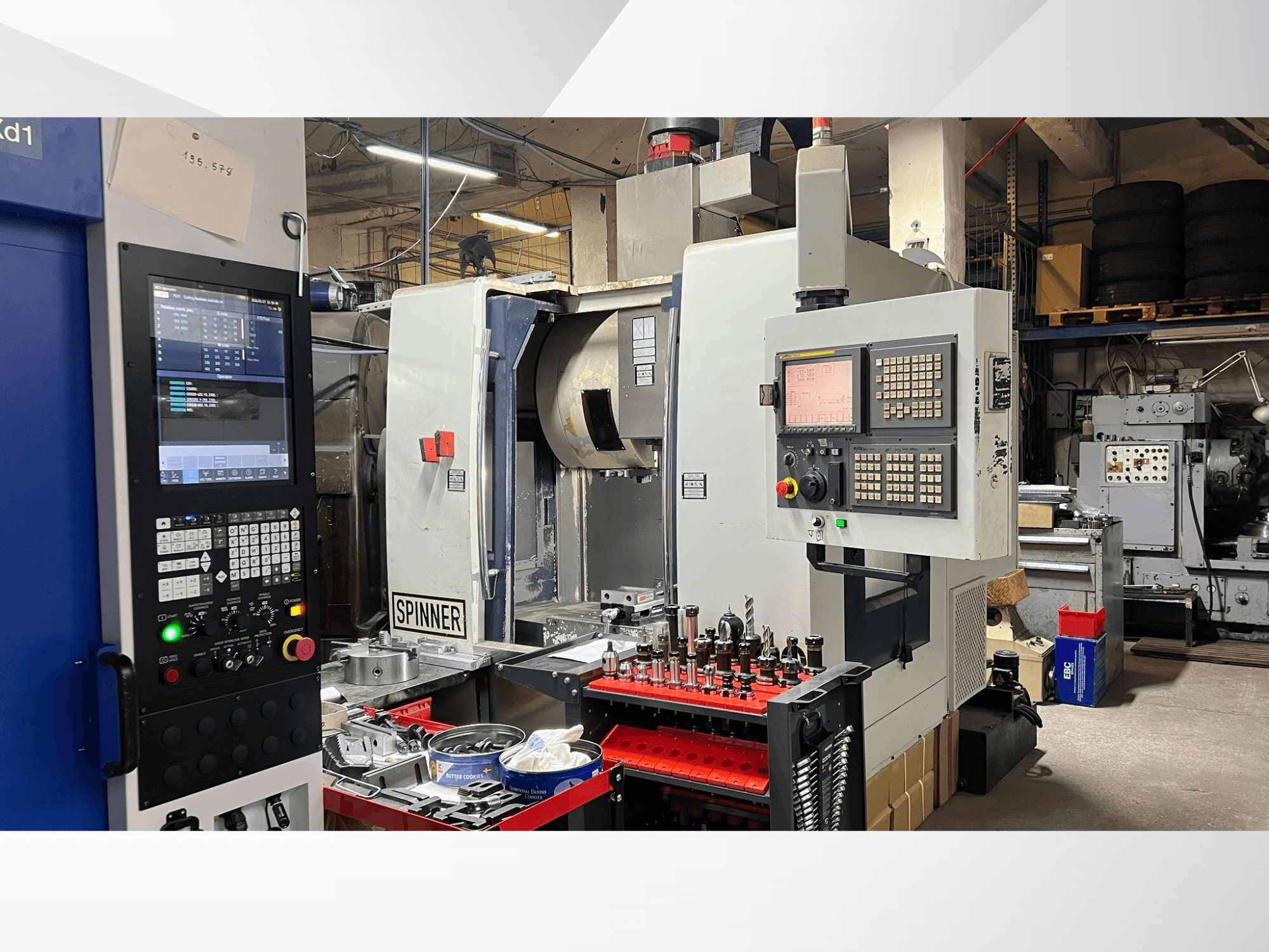 CNC staklės su matomu valdymo skydeliu, įrankiais ir ruošiniais, žiūrint iš priekio, dirbtuvių aplinkoje.