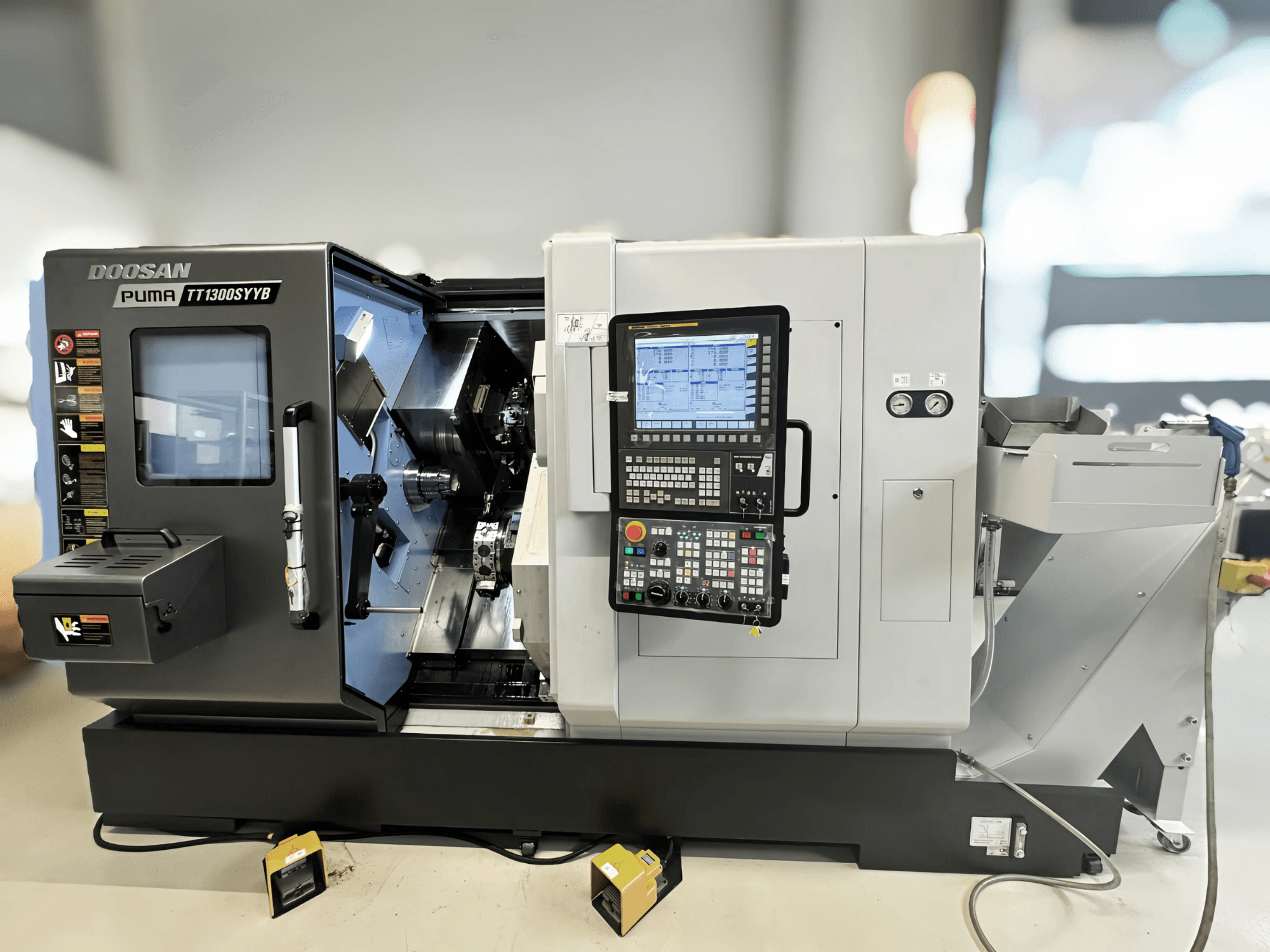 Doosan Puma TT1300SYYB tekinimo frezavimo centro šoninis vaizdas, matomas valdymo skydelis ir mašinos vidus su matomais įrankiais.
