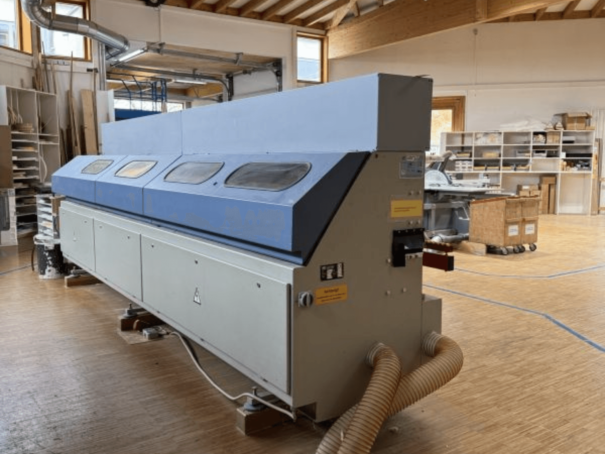 "OTT Pacific V6-F" kraštų šlifavimo staklės, parodytos iš šono; ilgas mėlynas viršus ir valdymo skydelis su žarnos tvirtinimo įtaisu.