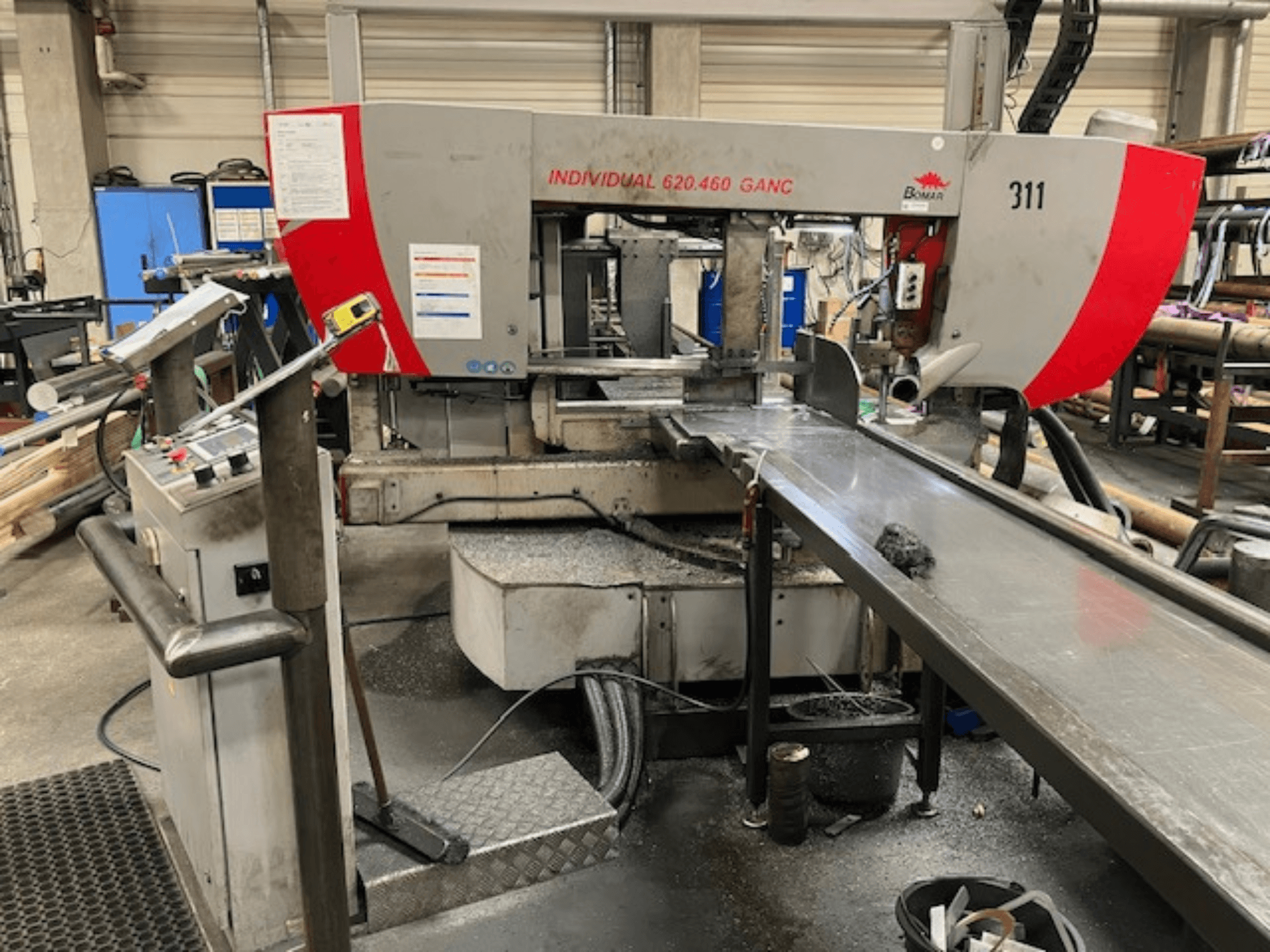 BOMAR INDIVIDUAL 620-460 GANC juostinis pjūklas, vaizdas iš priekio, kuriame matomi valdymo elementai, pjovimo zona ir pramoninių dirbtuvių fonas.