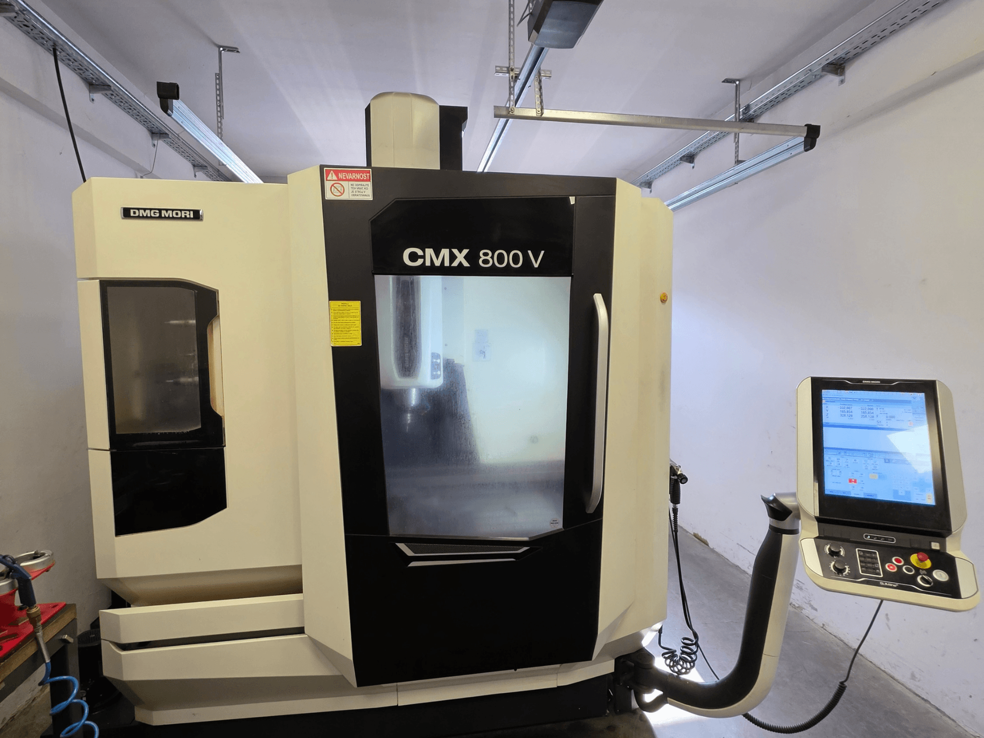 Vertikalusis apdirbimo centras „DMG MORI CMX 800V“, vaizdas iš priekio, su jutikliniu valdymo skydeliu ir aiškiais saugos ženklais.