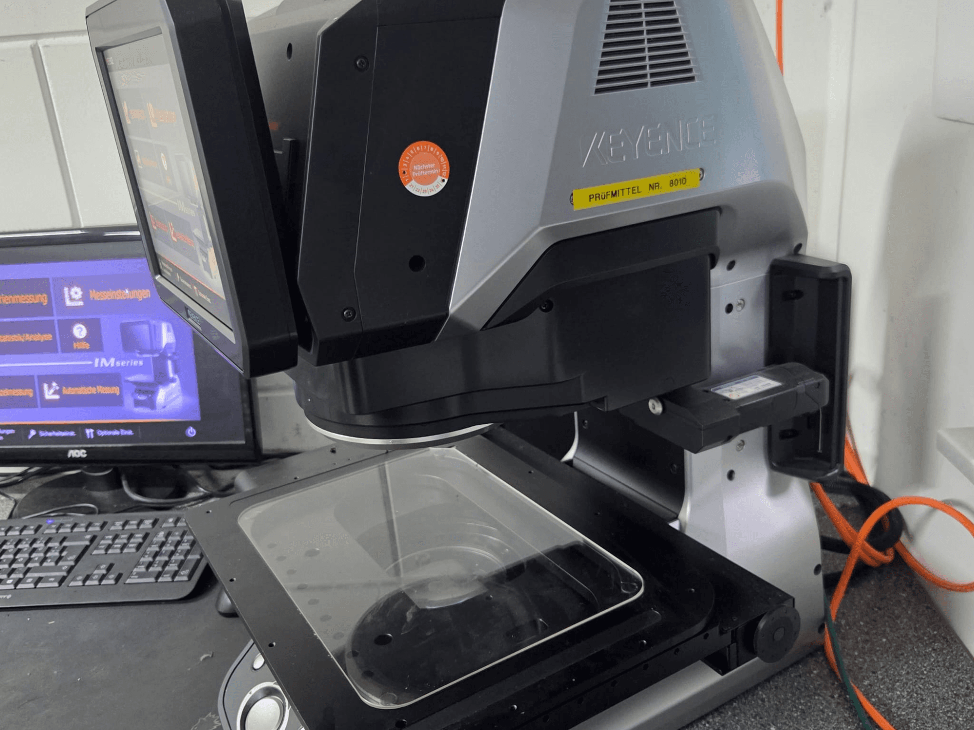 KEYENCE IM 7030 optinio matavimo mašina, vaizdas iš priekio su jutikliniu ekranu ir stikline matavimo plokštele.